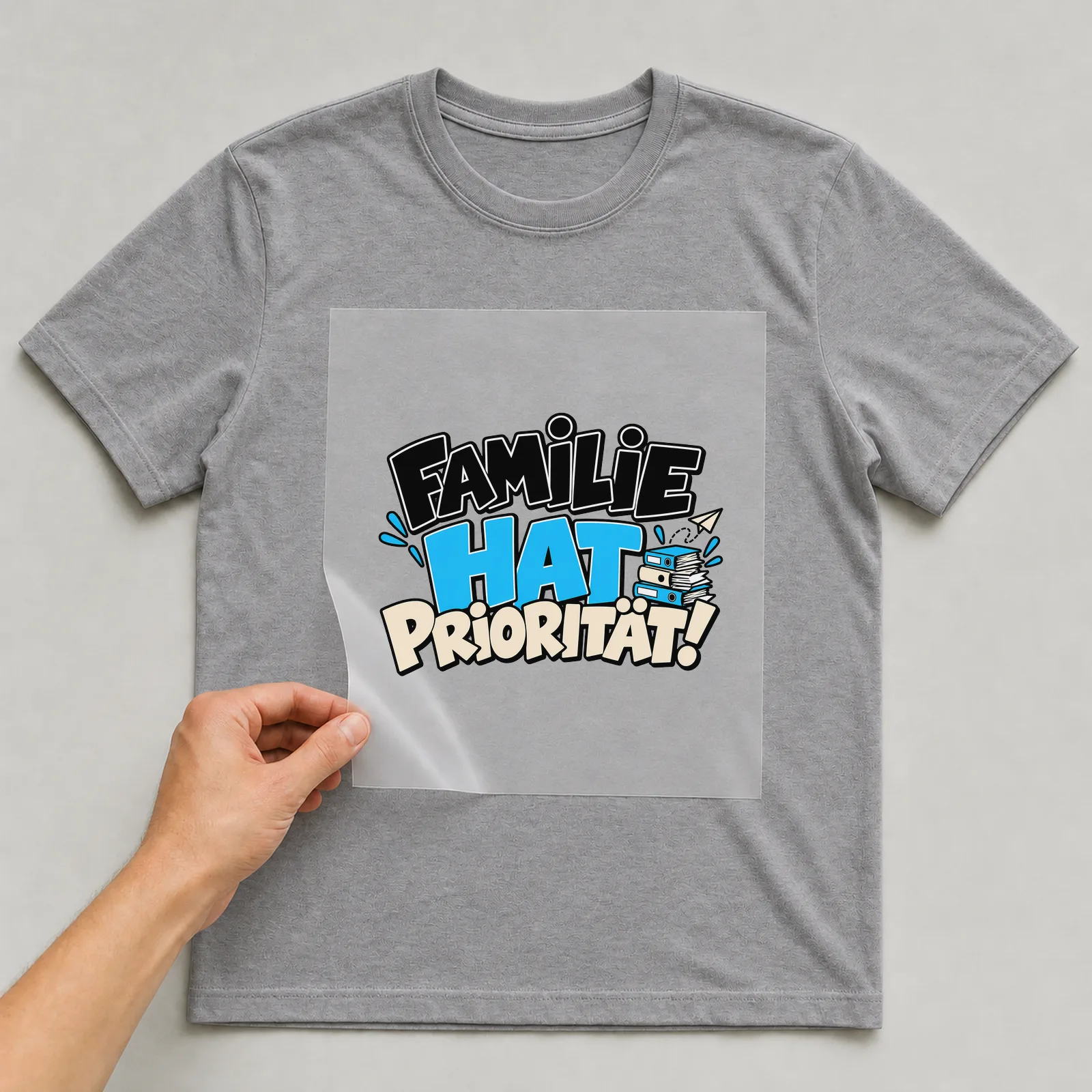 Bügelbild „Familie hat Priorität!“ auf grauem T-Shirt, Folie wird aufgelegt