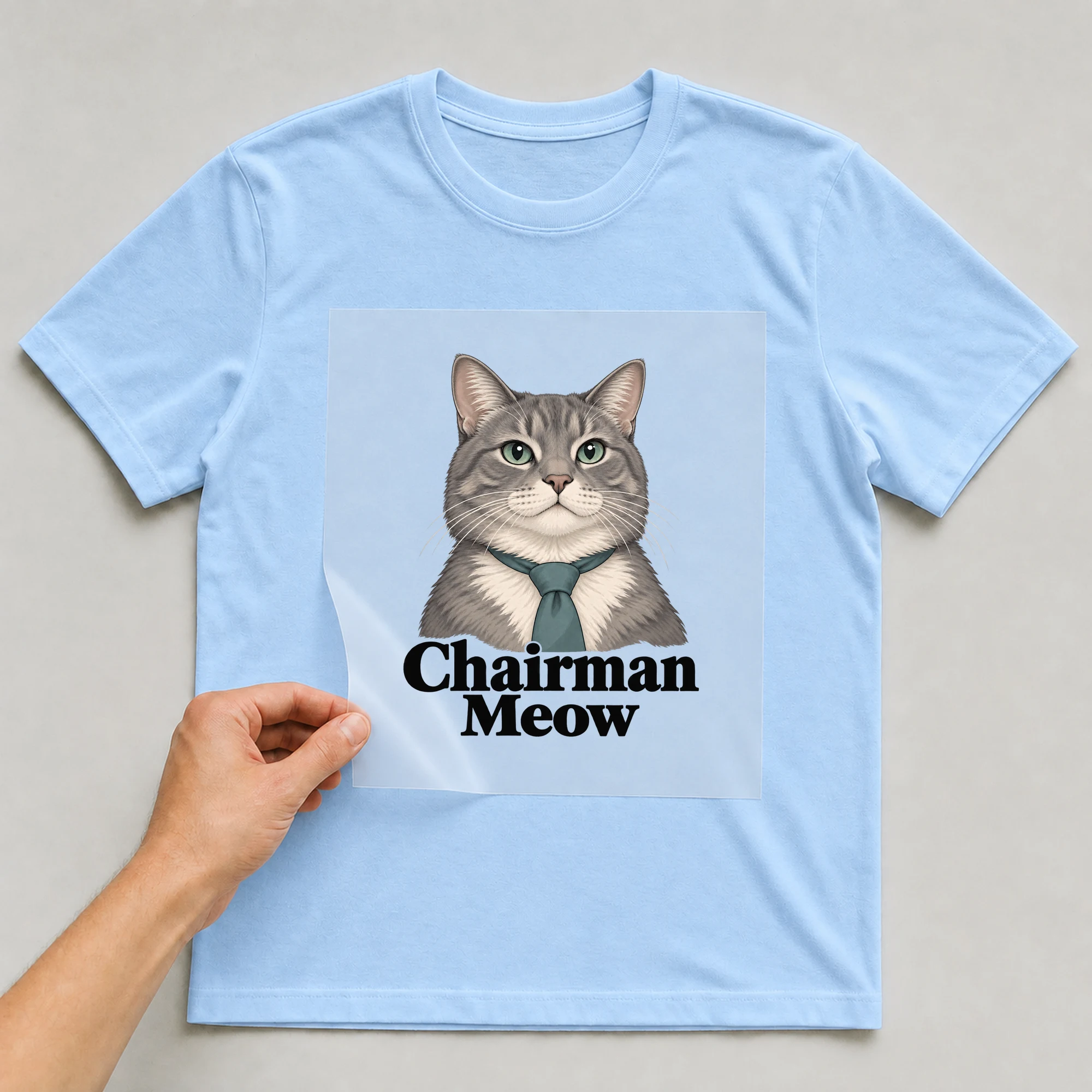 Bügelbild „Chairman Meow“ auf babyblauem T-Shirt, Folie wird aufgelegt