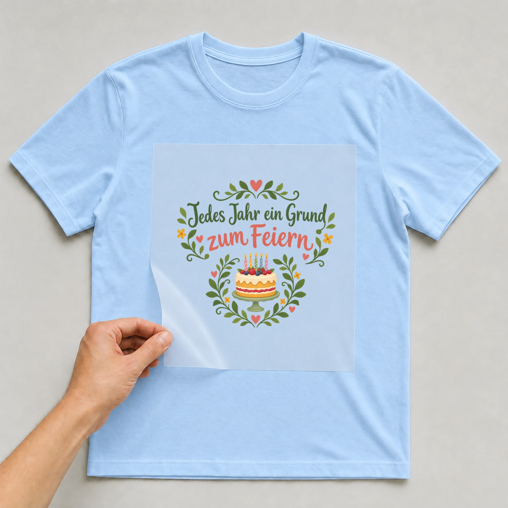 Bügelbild „Jedes Jahr ein Grund zum Feiern“ auf babyblauem T-Shirt, Folie wird aufgelegt