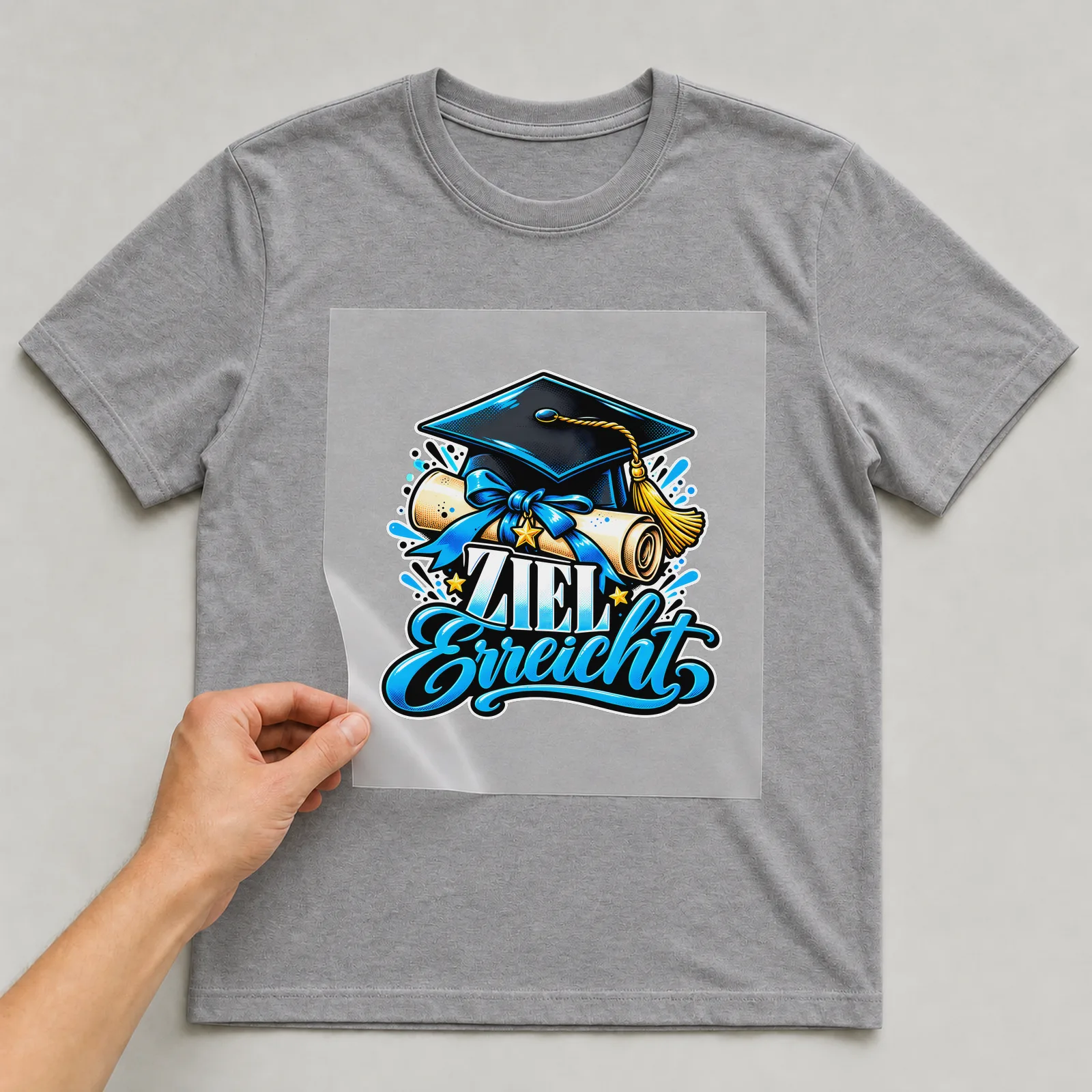 Bügelbild „Ziel erreicht“ auf grauem T-Shirt, Folie wird aufgelegt