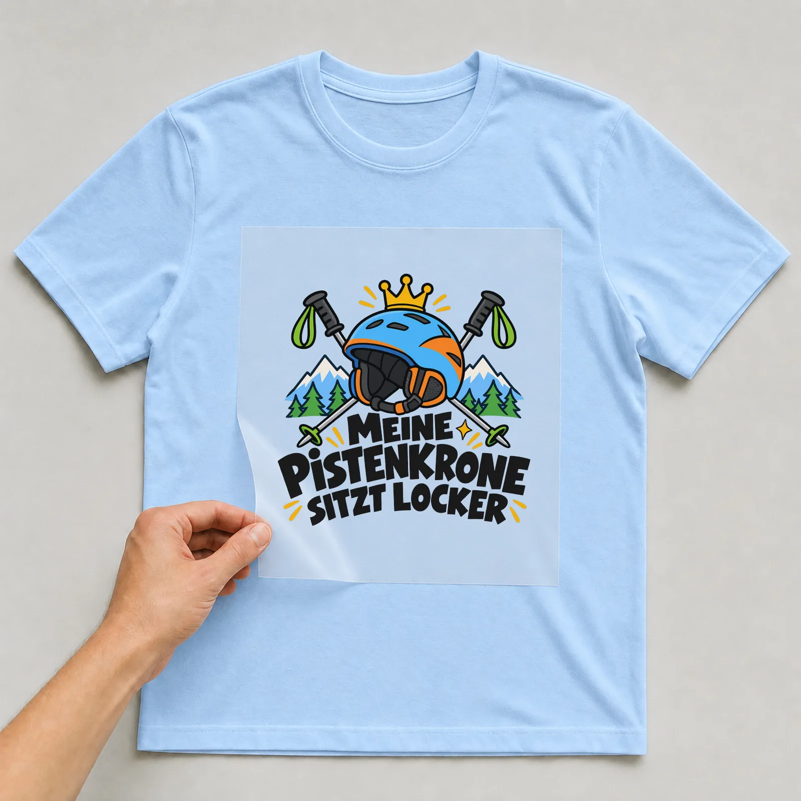 Bügelbild „Meine Pistenkrone sitzt locker“ auf hellblauem T-Shirt, Folie wird aufgelegt