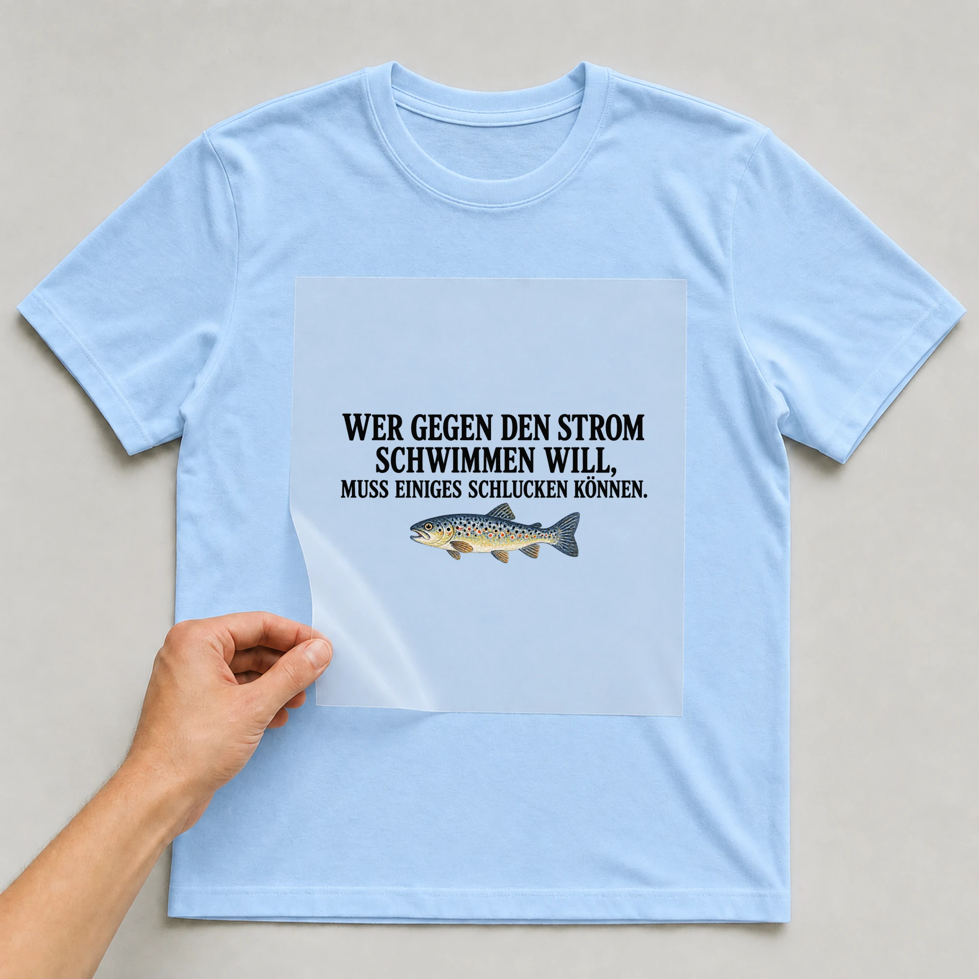 Bügelbild „Wer gegen den Strom schwimmen will, muss einiges schlucken können.“ auf babyblauem T-Shirt, Folie wird aufgelegt