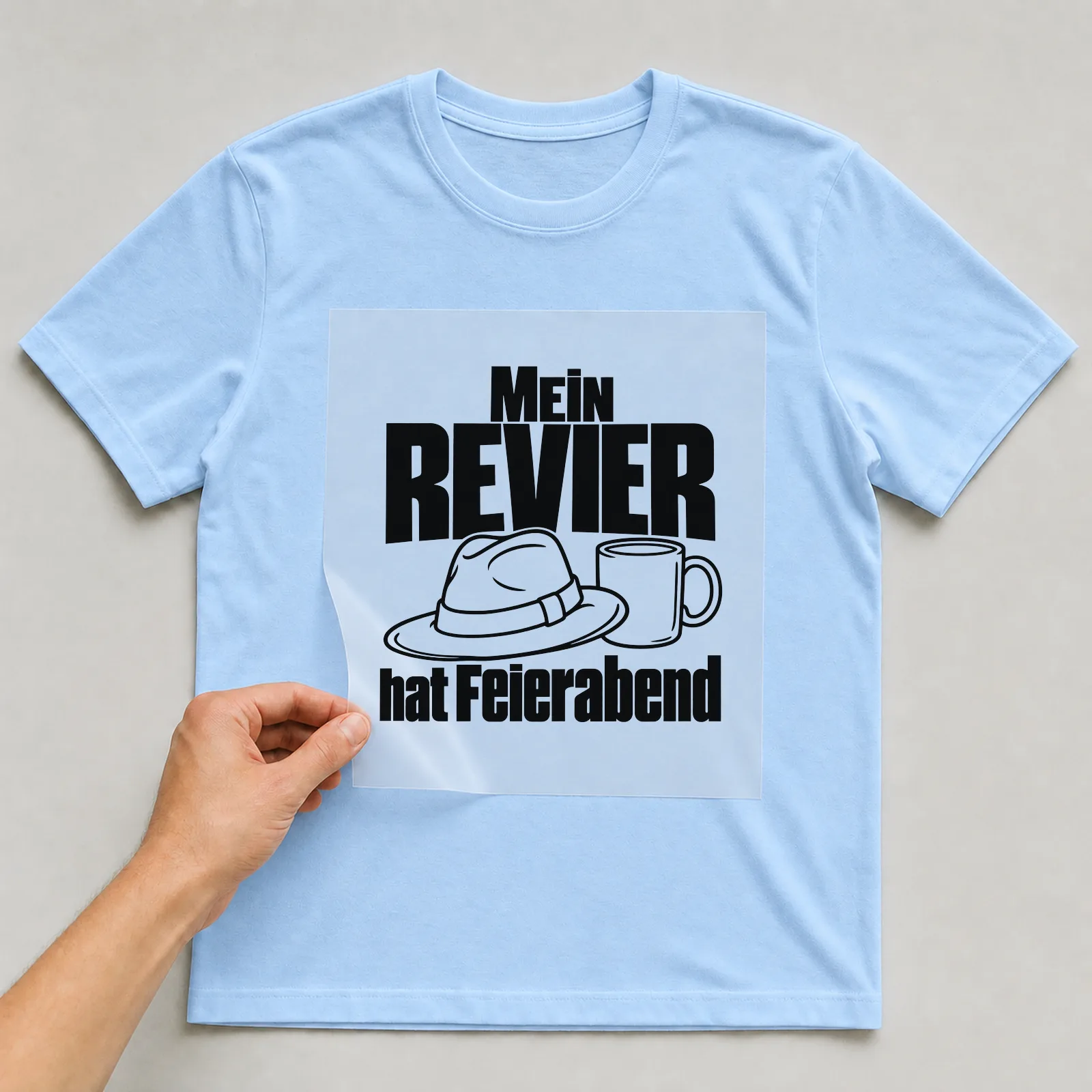 Bügelbild „Mein Revier hat Feierabend“ auf hellblauem T-Shirt, Folie wird aufgelegt