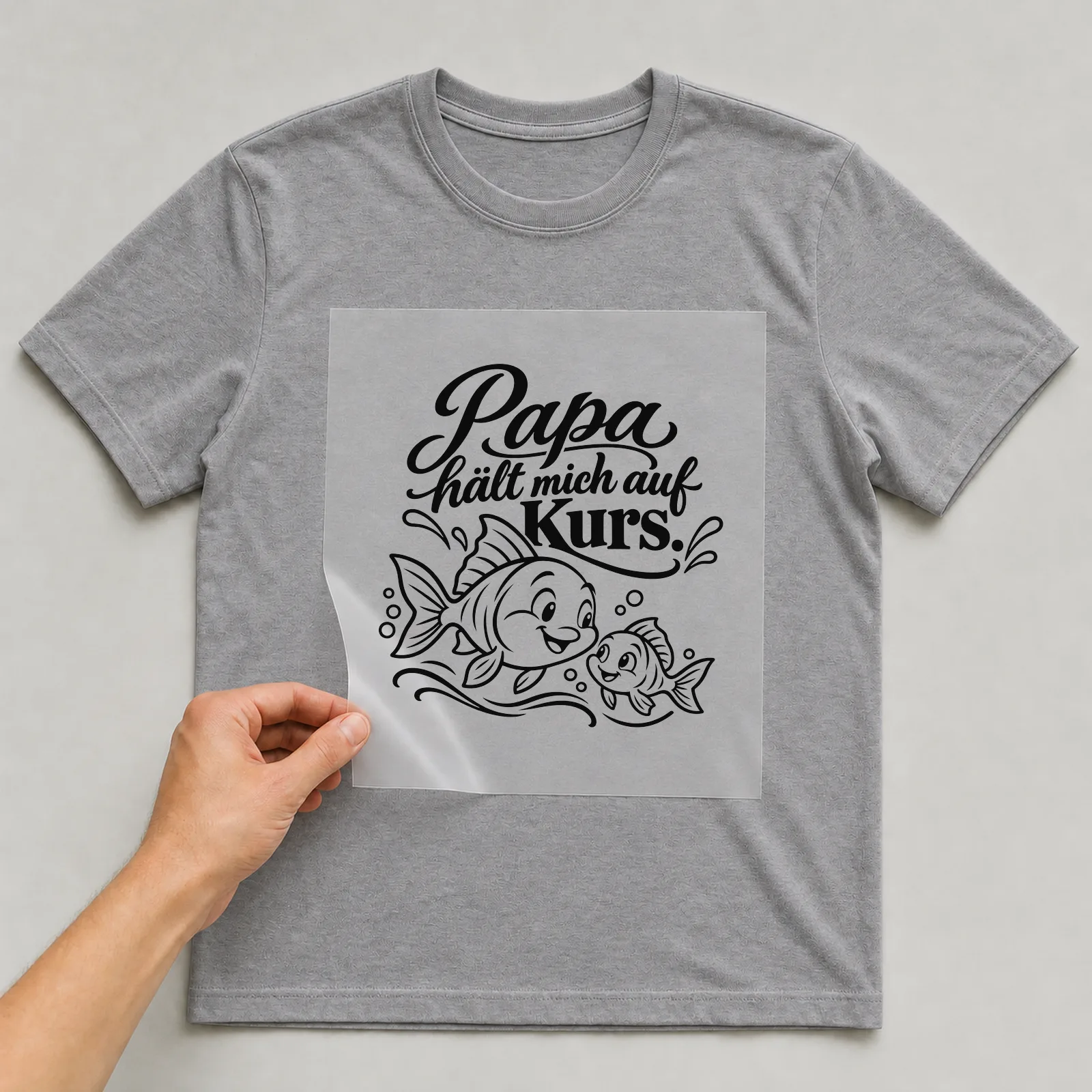Bügelbild „Papa hält mich auf Kurs“ auf grauem T-Shirt, Folie wird aufgelegt