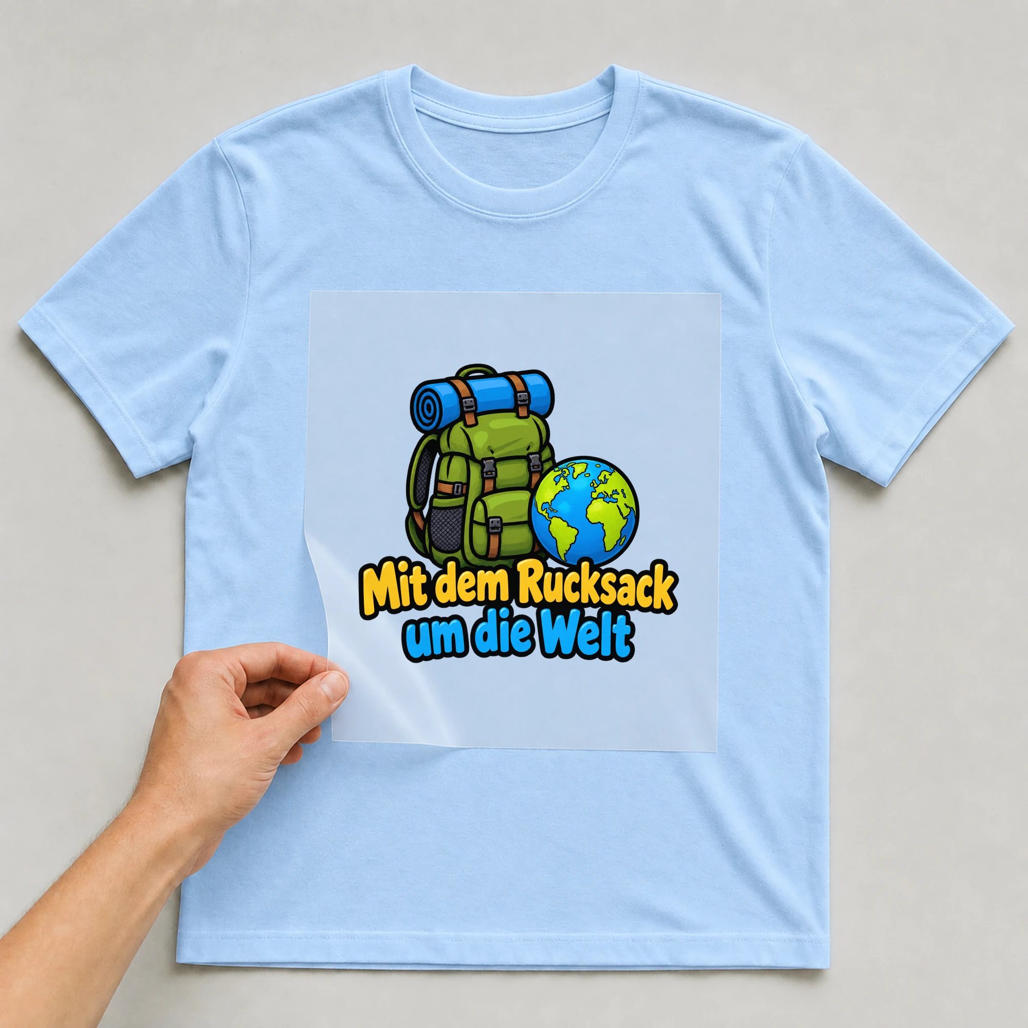 Bügelbild „Mit dem Rucksack um die Welt“ auf babyblauem T-Shirt, Folie wird aufgelegt