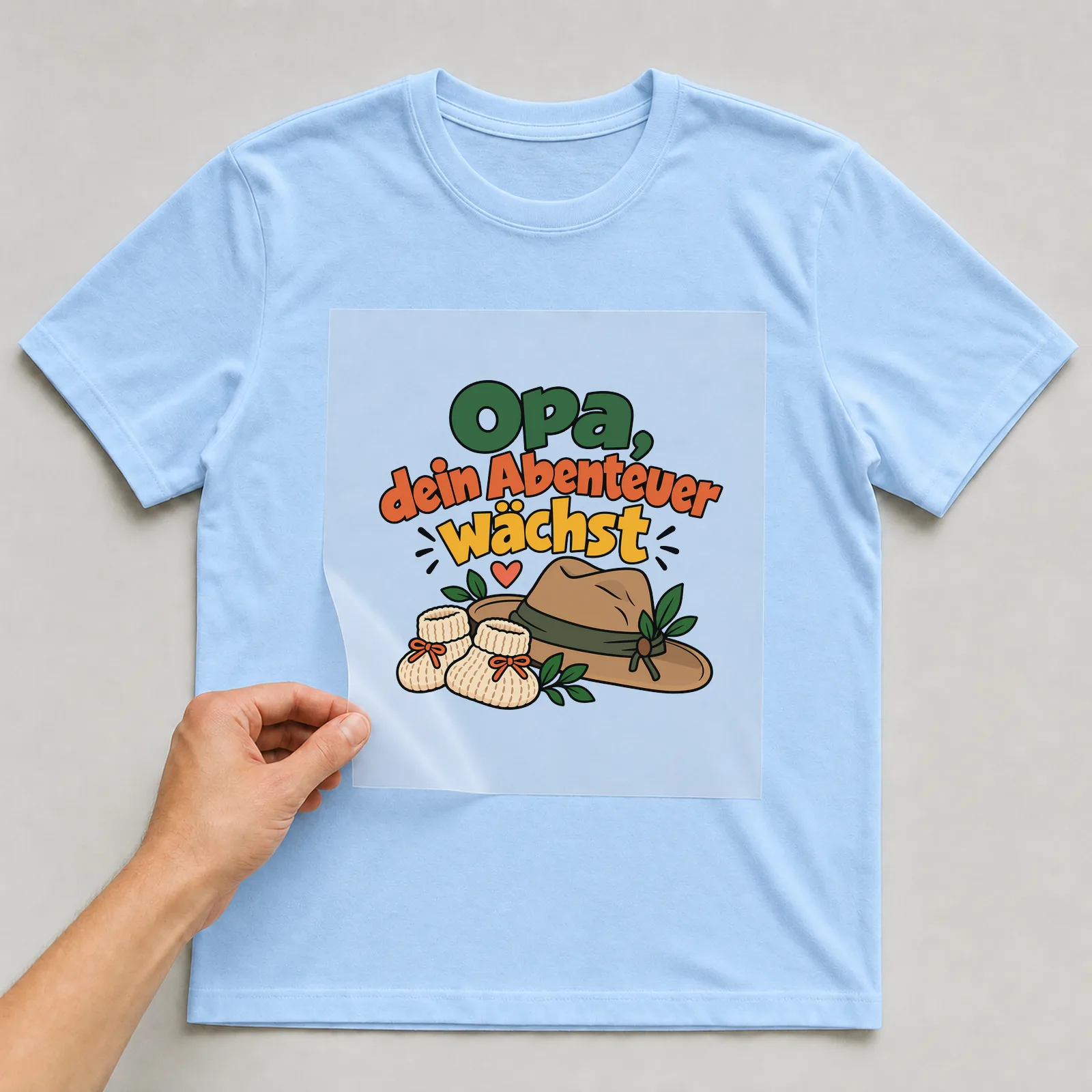 Bügelbild „Opa, dein Abenteuer wächst“ auf hellblauem T-Shirt, Folie wird aufgelegt