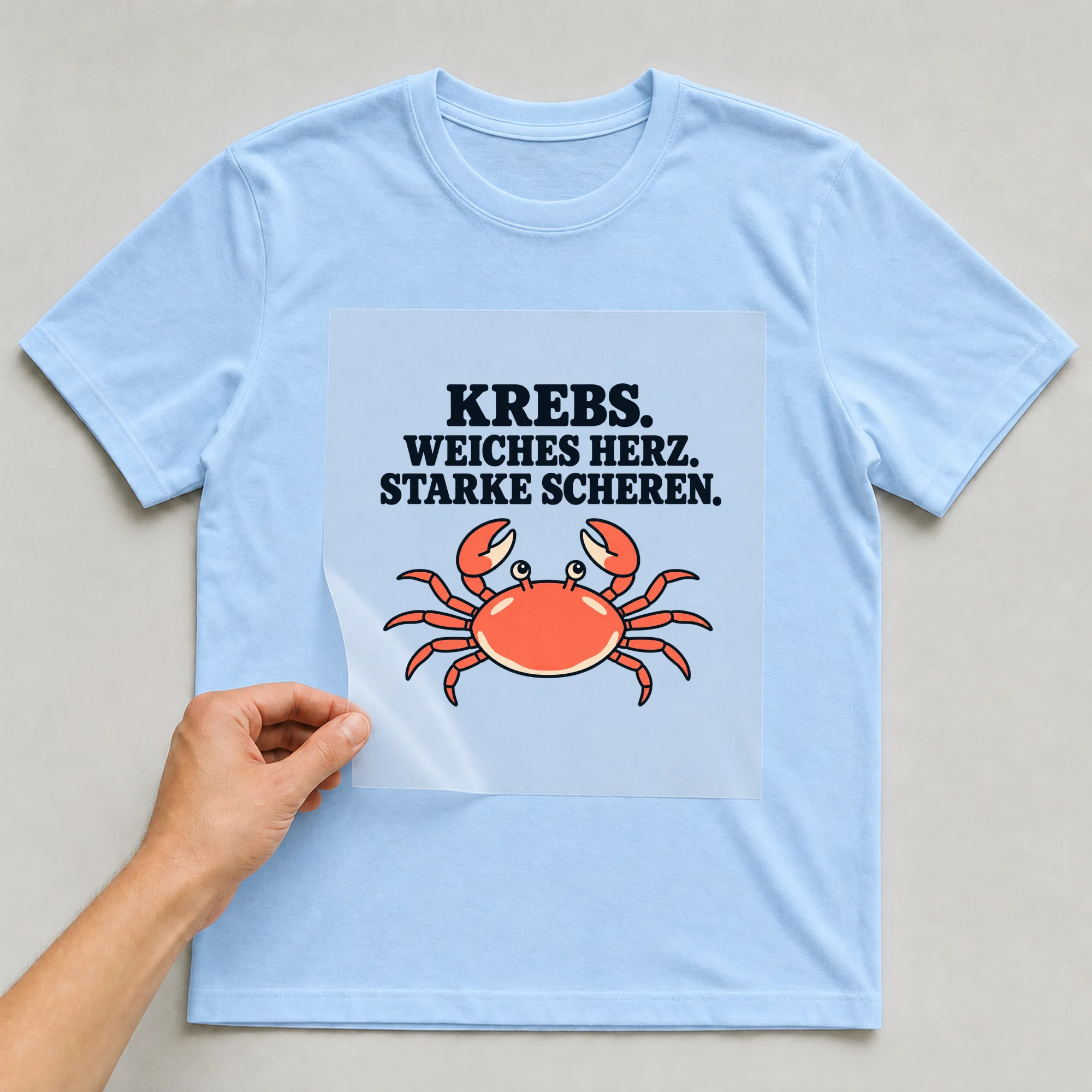 Bügelbild „KREBS. WEICHES HERZ. STARKE SCHEREN.“ auf babyblauem T-Shirt, Folie wird aufgelegt