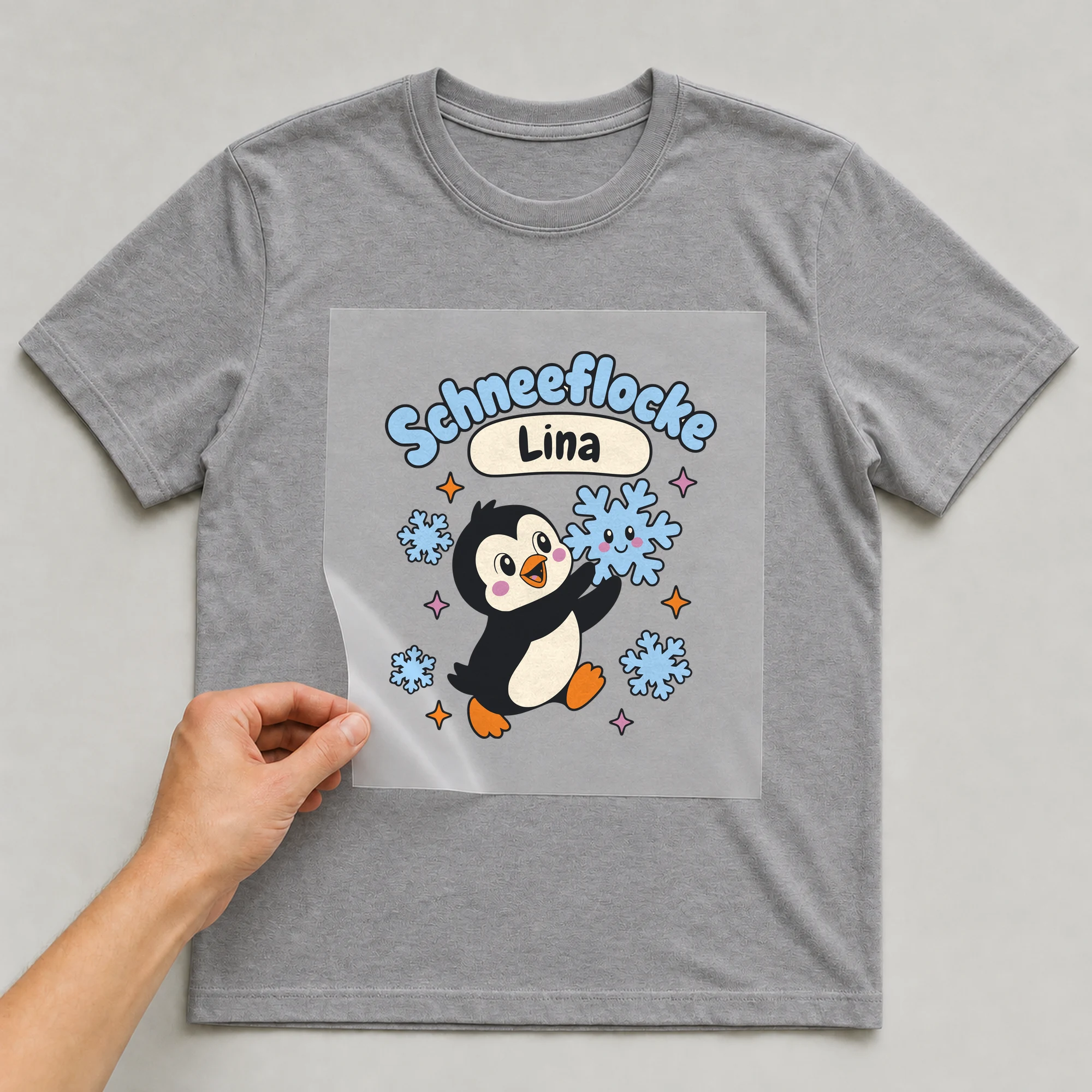 Bügelbild Schneeflocke mit Name auf grauem T-Shirt, Folie wird aufgelegt