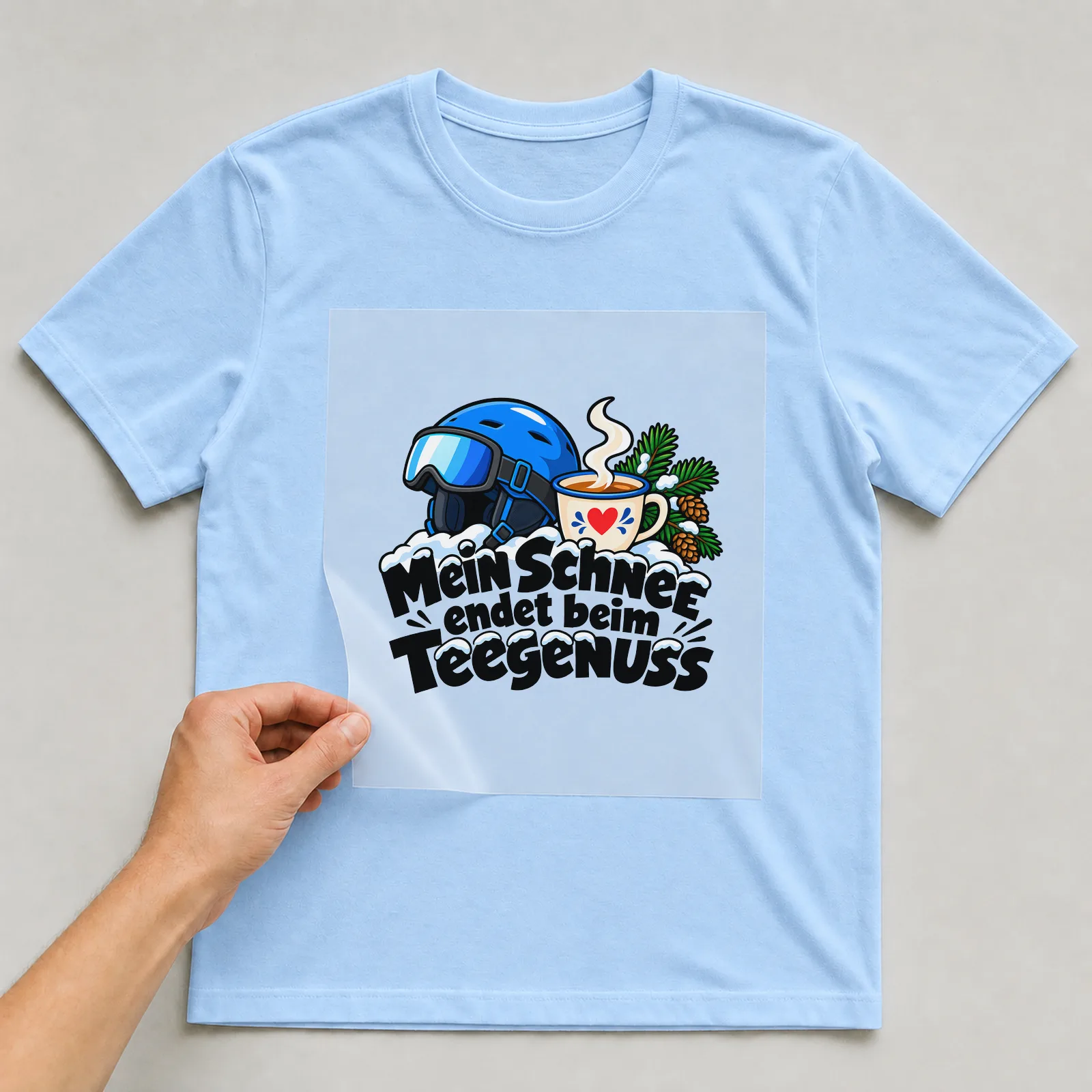 Bügelbild „Mein Schnee endet beim Teegenuss“ auf hellblauem T-Shirt, Folie wird aufgelegt