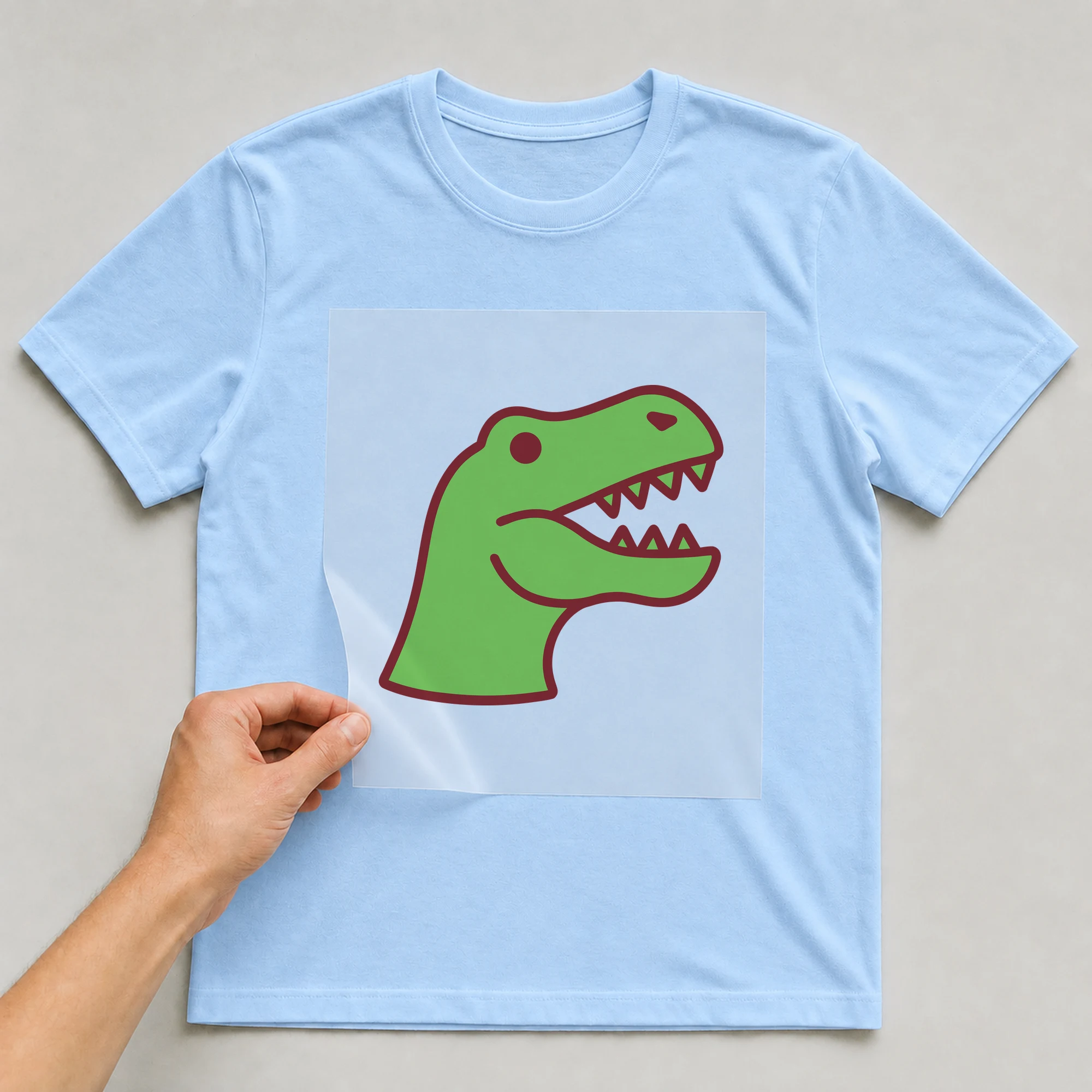 Bügelbild „Dino-Kopf“ auf babyblauem T-Shirt, Folie wird aufgelegt