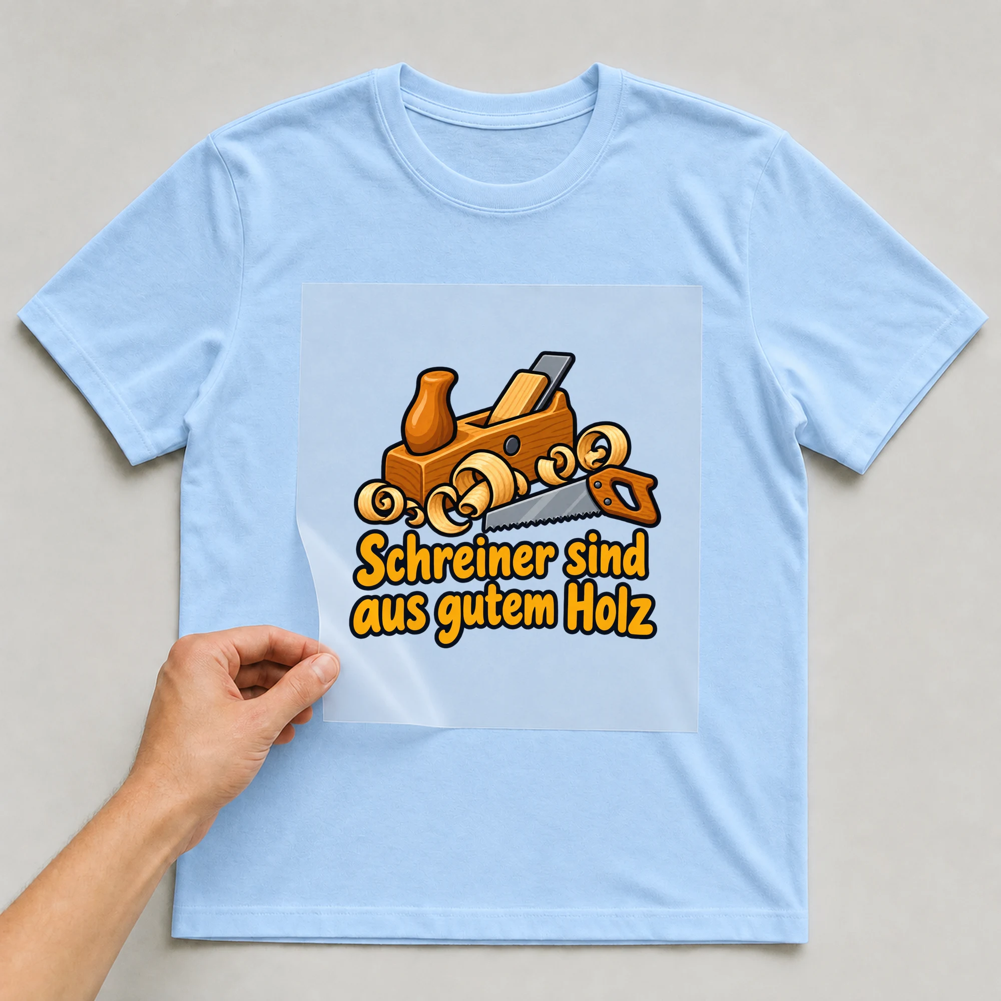 Bügelbild „Schreiner sind aus gutem Holz“ auf babyblauem T-Shirt, Folie wird aufgelegt