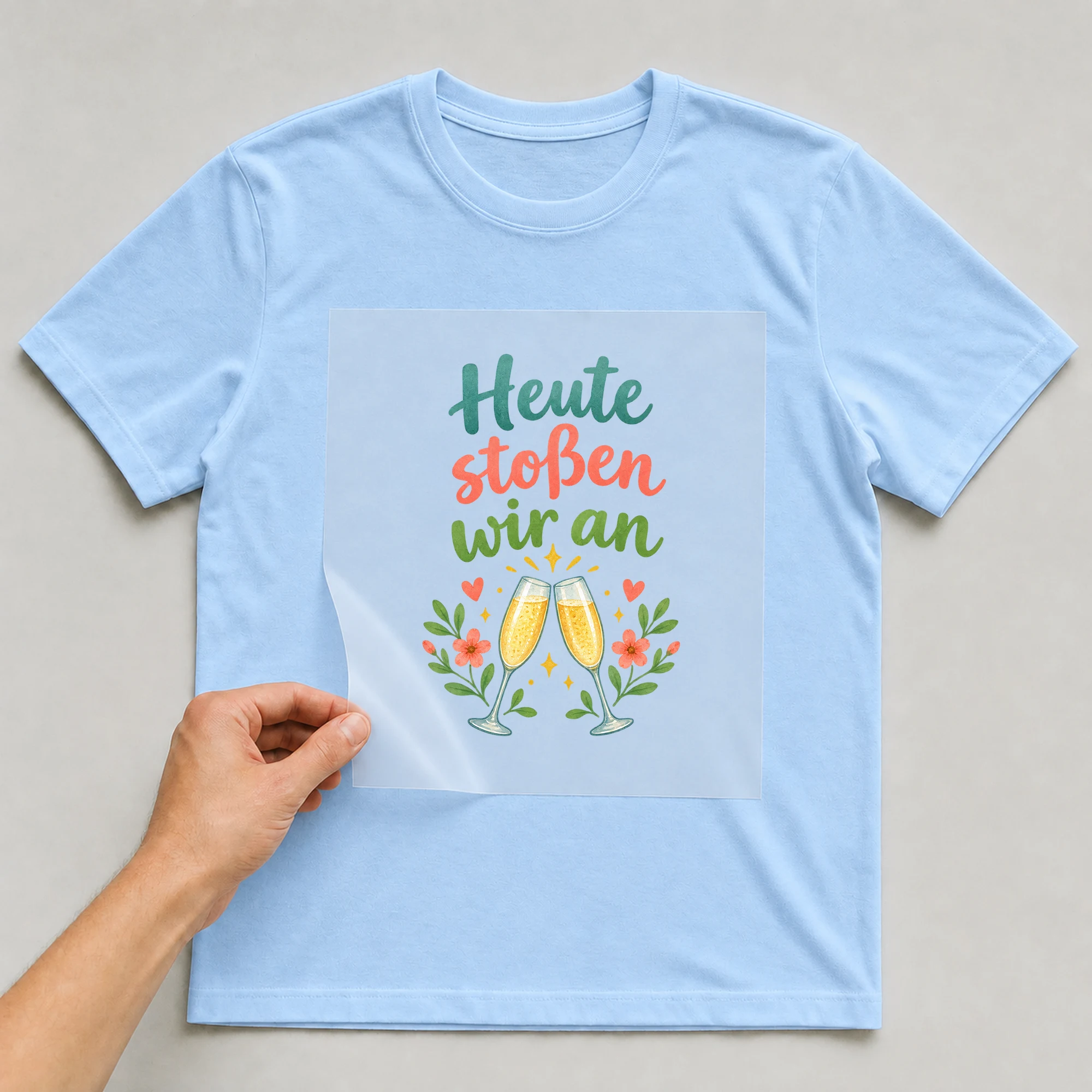 Bügelbild „Heute stoßen wir an“ auf babyblauem T-Shirt, Folie wird aufgelegt