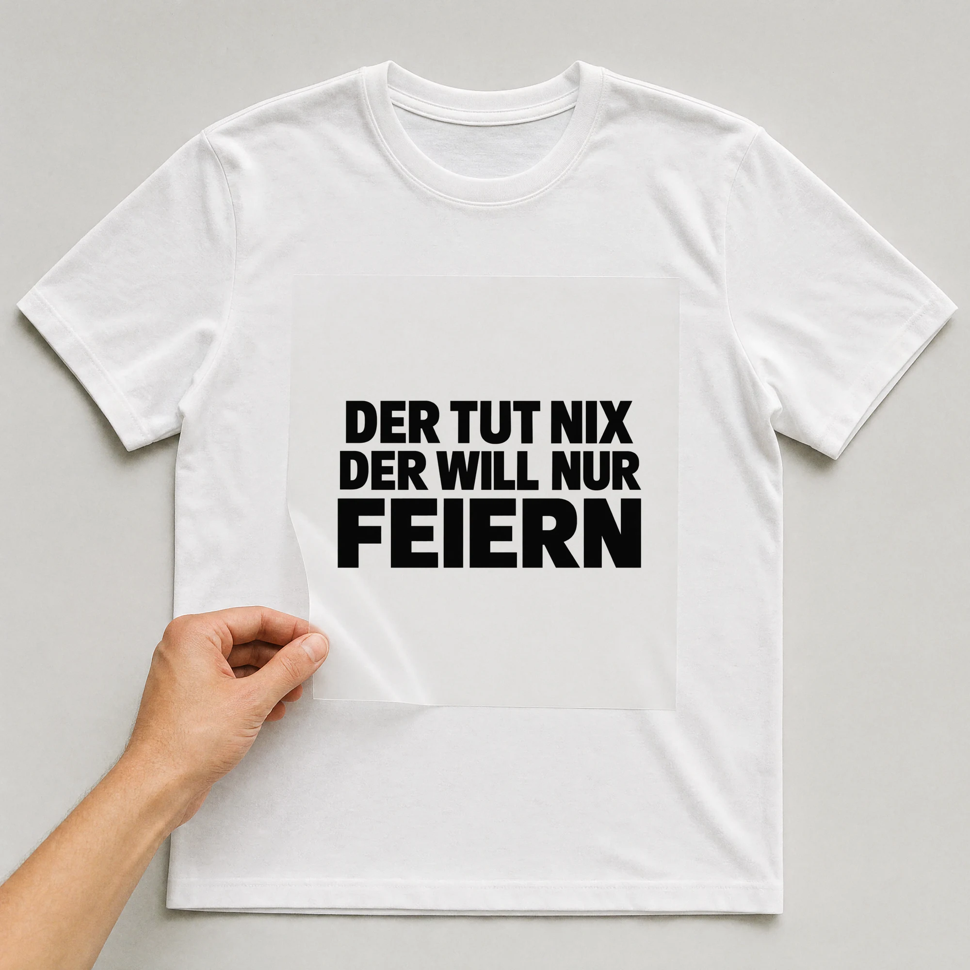 Bügelbild „Der tut nix der will nur feiern“ auf weißem T-Shirt, Folie wird aufgelegt