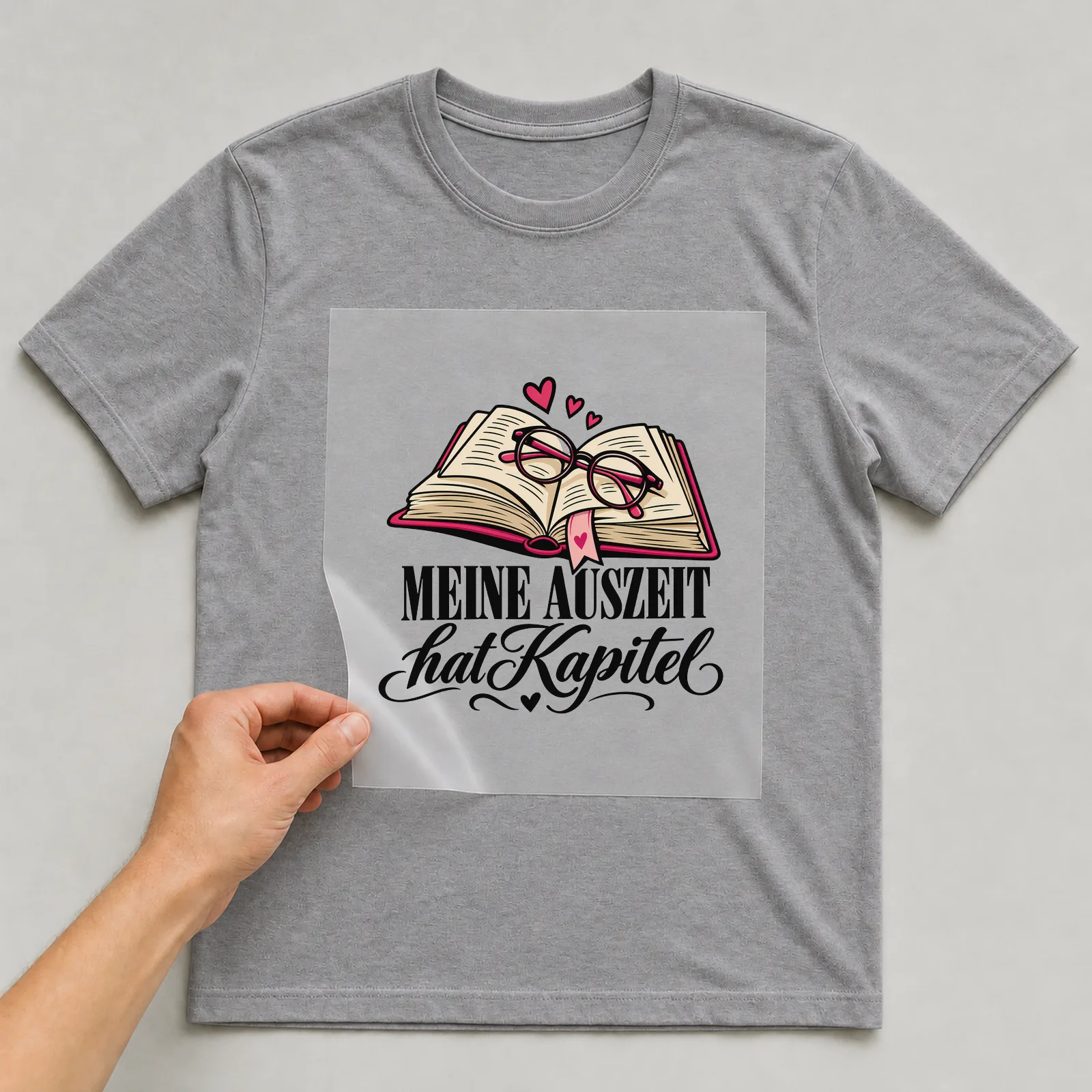 Bügelbild „Meine Auszeit hat Kapitel“ auf grauem T-Shirt, Folie wird aufgelegt
