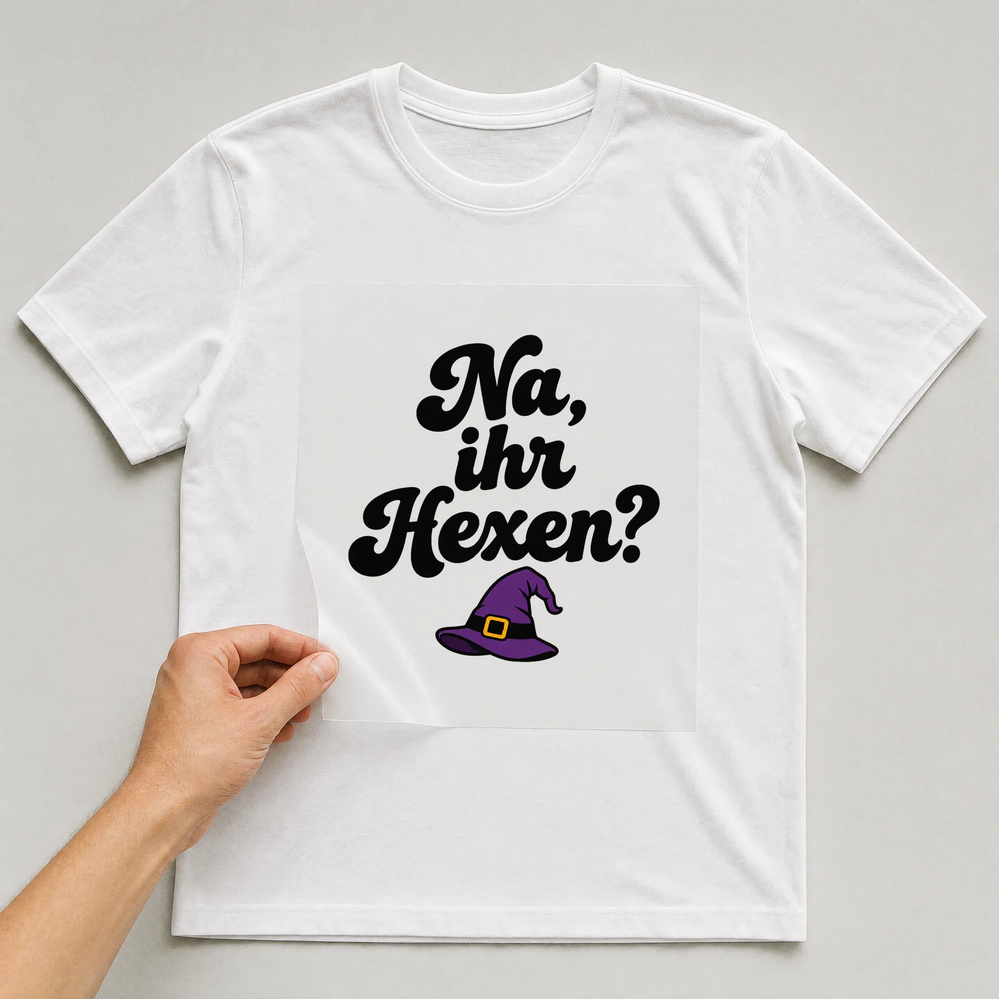 Bügelbild „Na, ihr Hexen?“ auf weißem T-Shirt, Folie wird aufgelegt