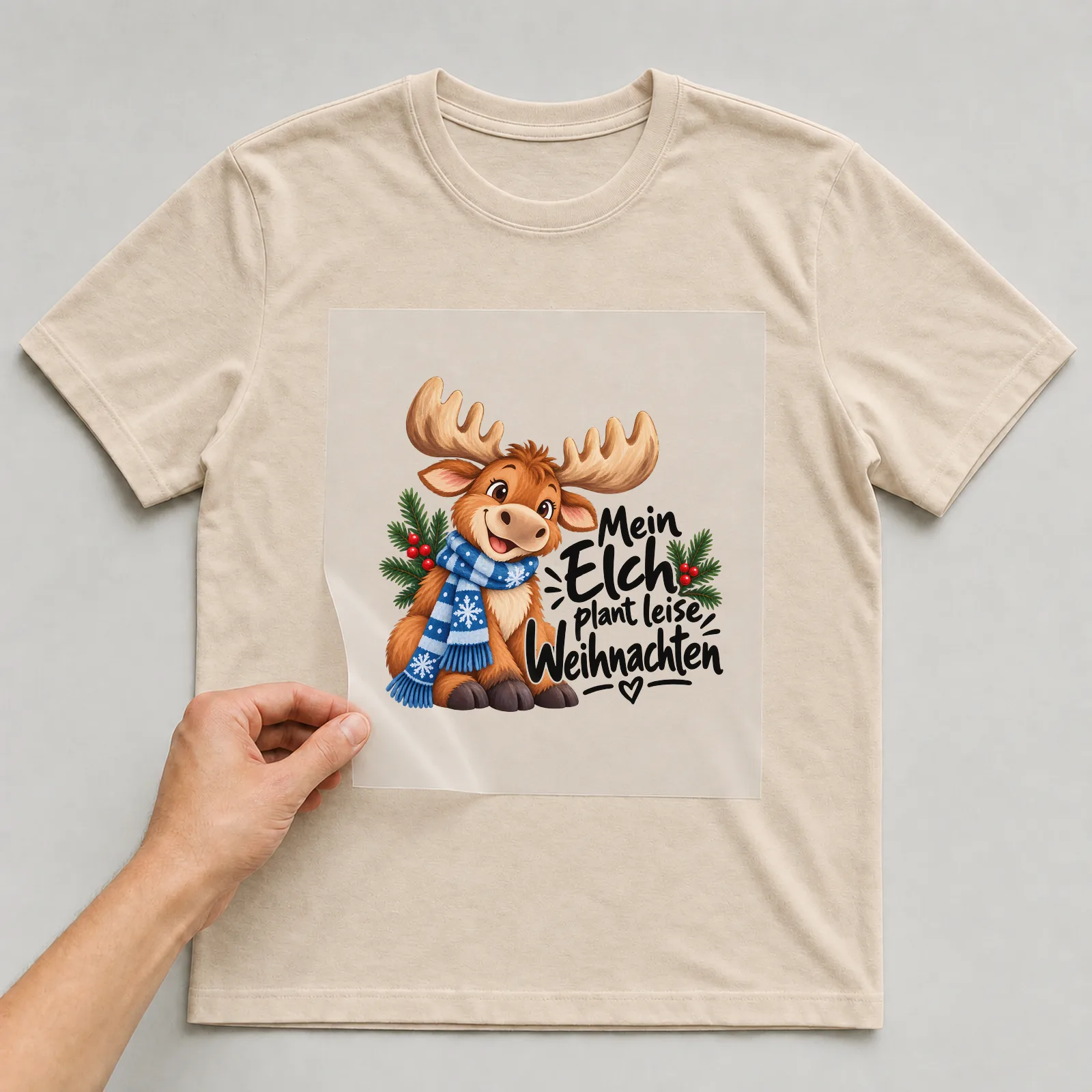 Bügelbild „Mein Elch plant leise Weihnachten“ auf beigem T-Shirt, Folie wird aufgelegt