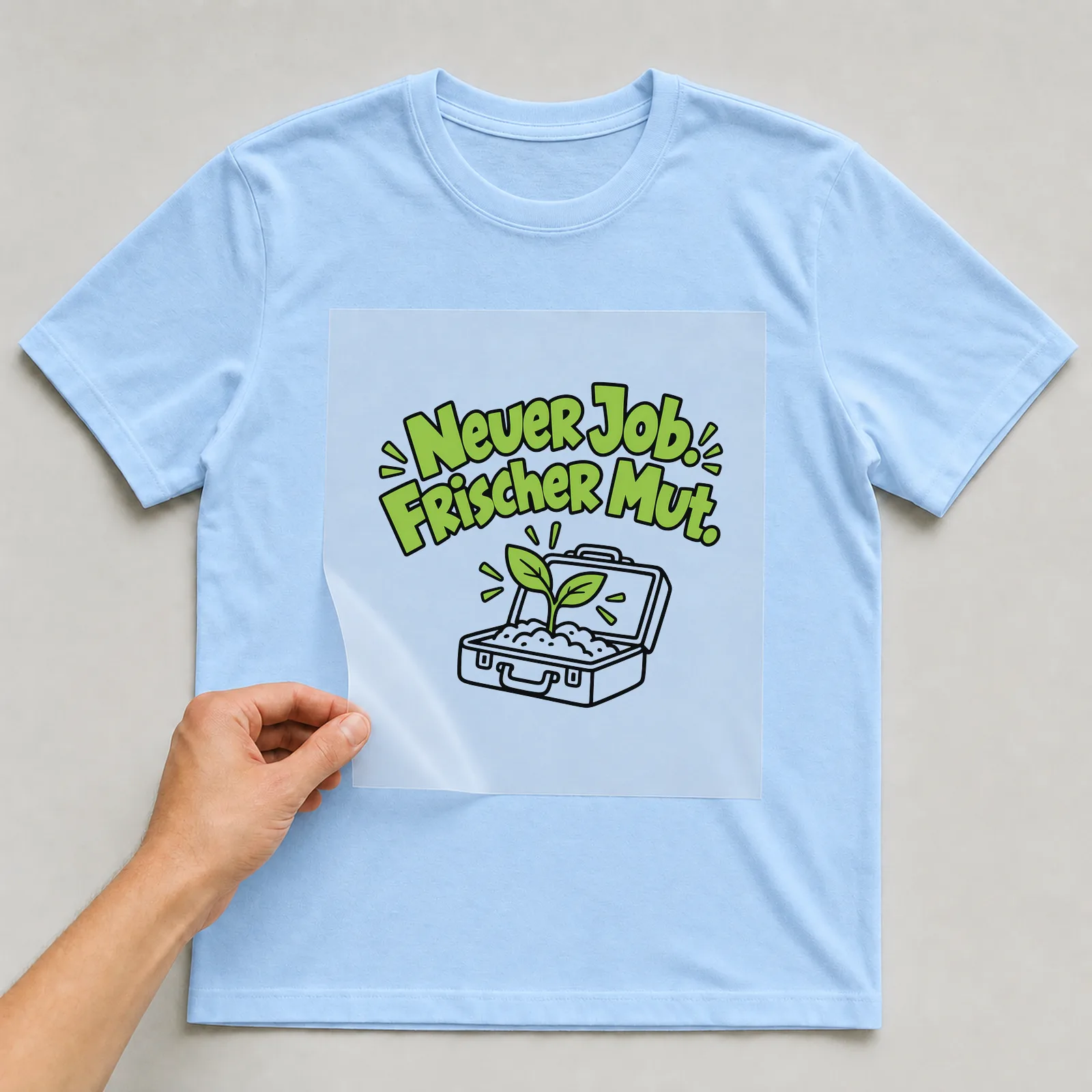 Bügelbild „Neuer Job. Frischer Mut.“ auf hellblauem T-Shirt, Folie wird aufgelegt