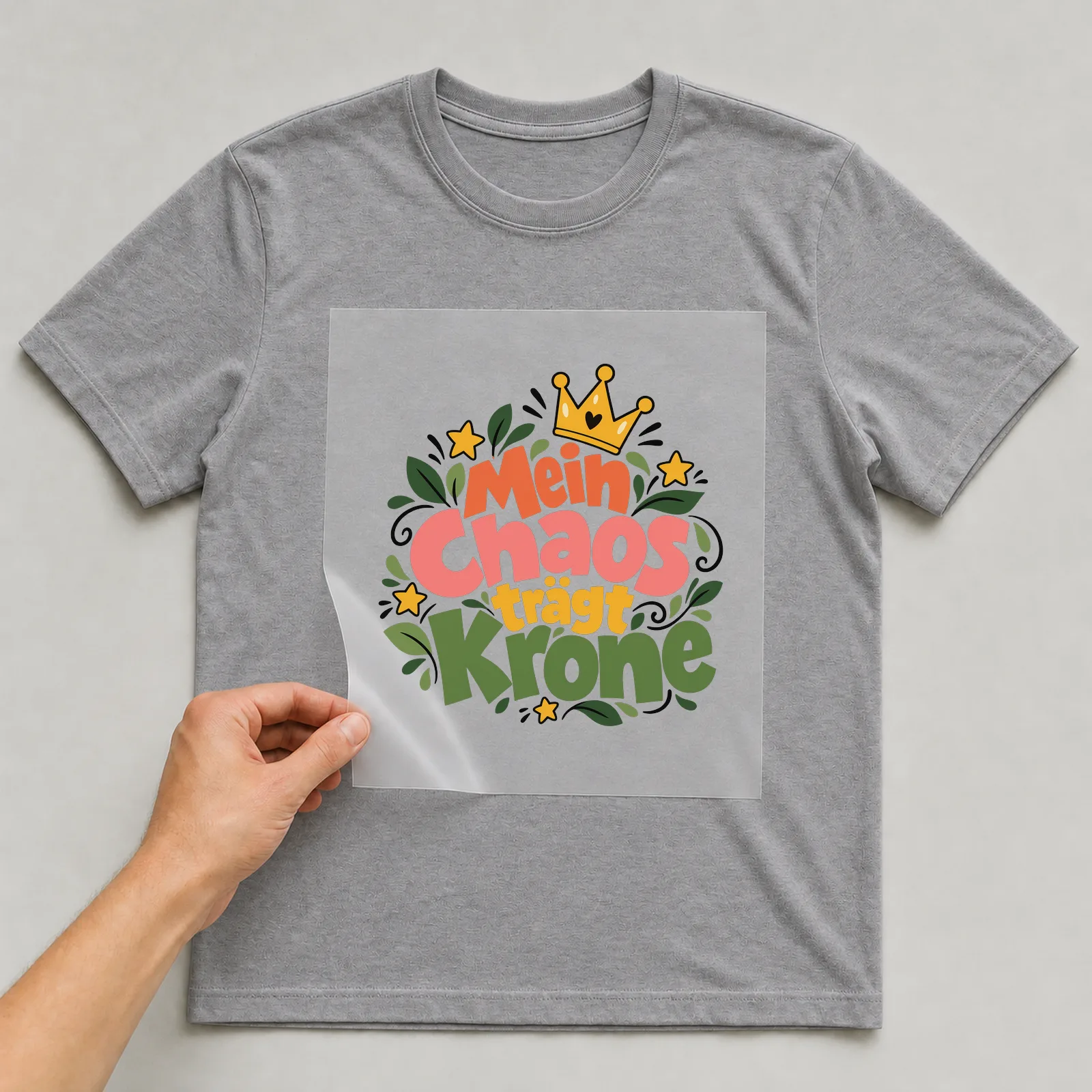 Bügelbild „Mein Chaos trägt Krone“ auf grauem T-Shirt, Folie wird aufgelegt
