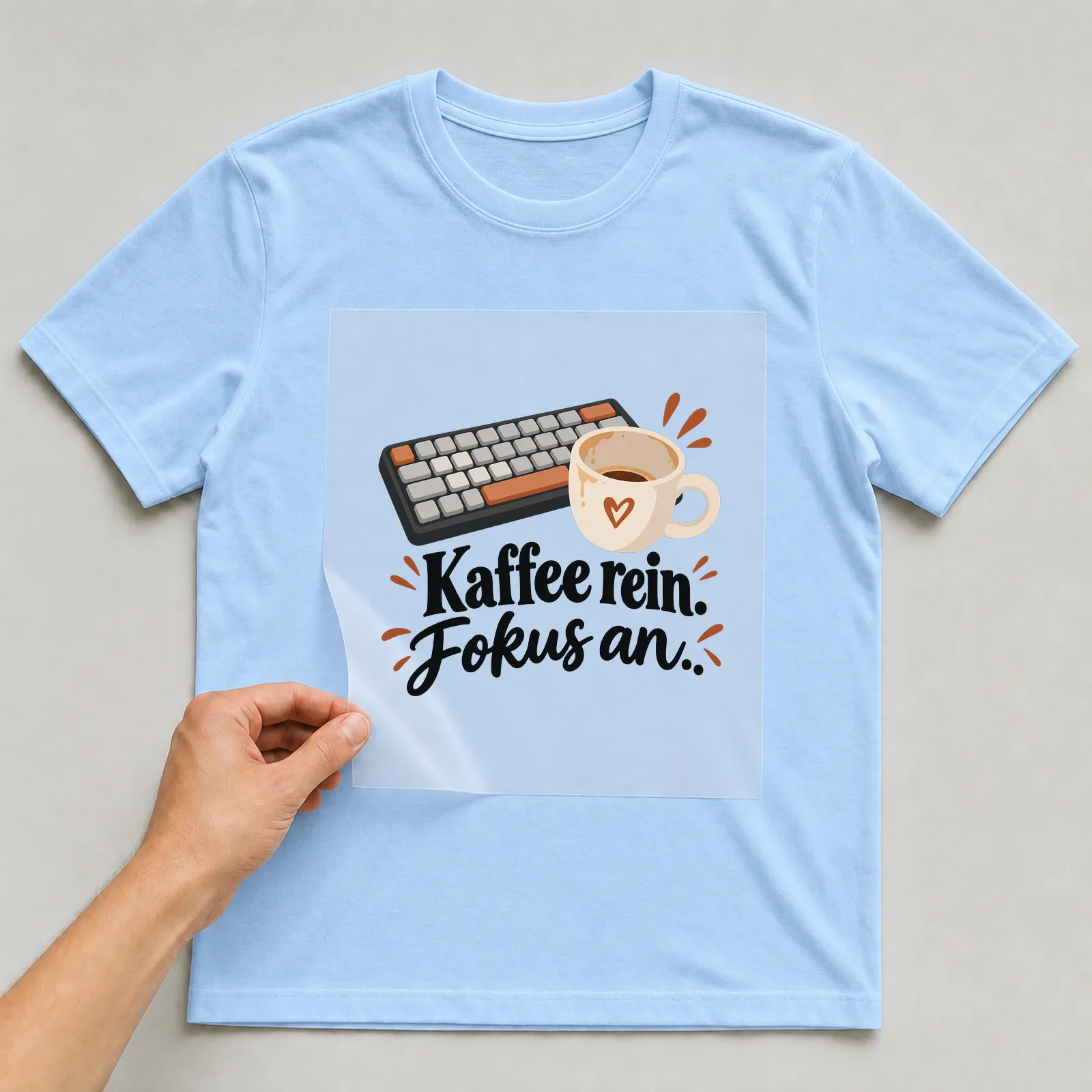 Bügelbild „Kaffee rein. Fokus an.“ auf hellblauem T-Shirt, Folie wird aufgelegt