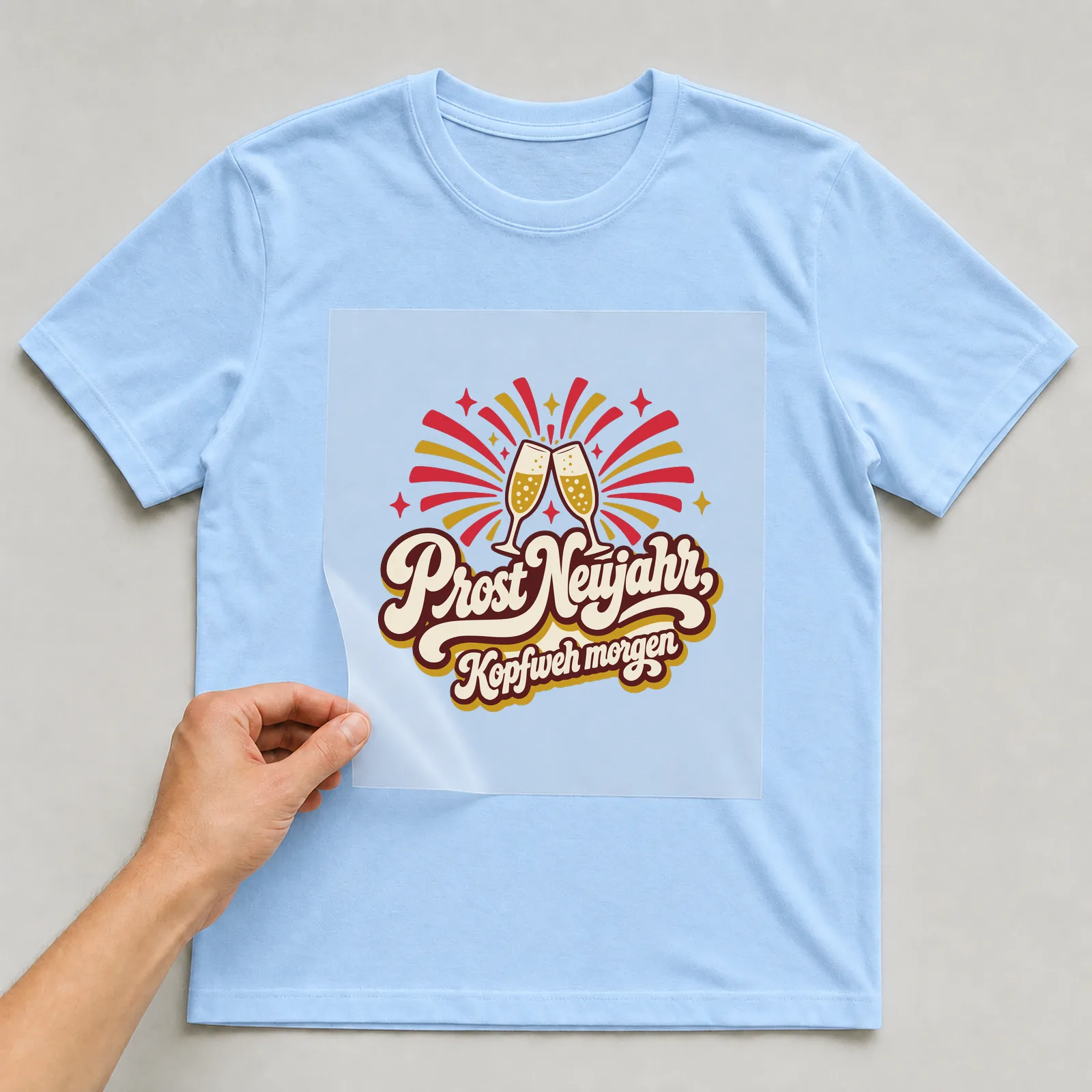 Bügelbild Prost Neujahr, Kopfweh morgen auf hellblauem T-Shirt, Folie wird aufgelegt