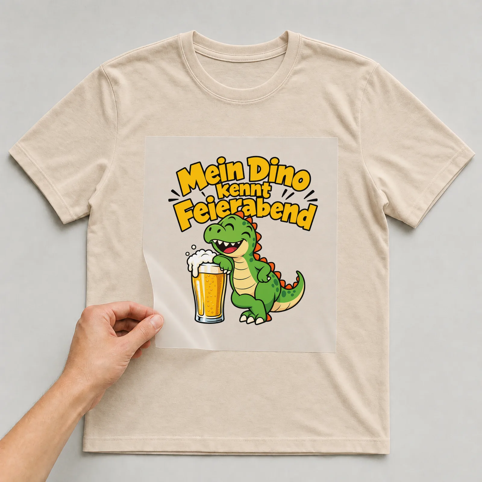 Bügelbild „Mein Dino kennt Feierabend“ auf beigem T-Shirt, Folie wird aufgelegt