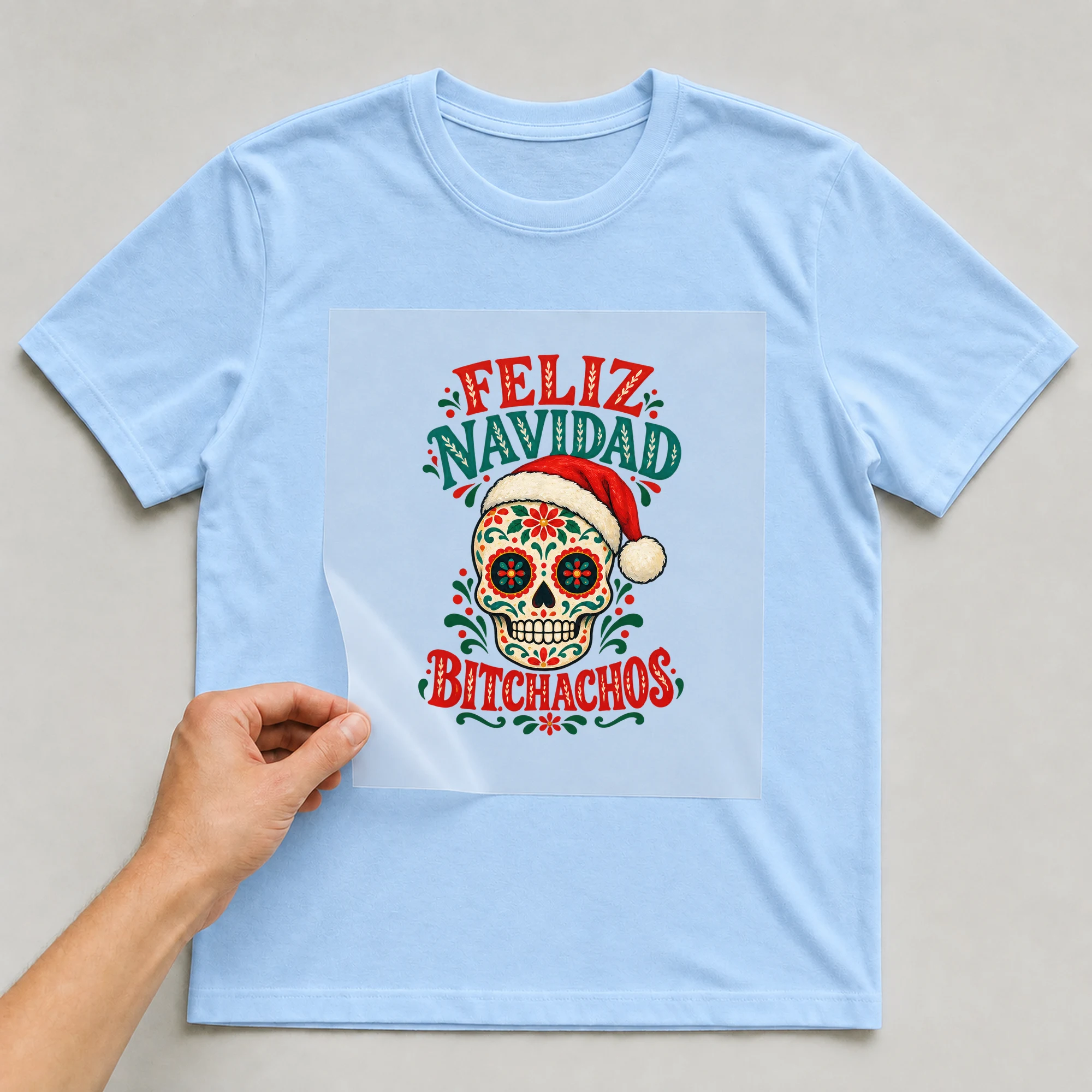 Bügelbild „Feliz Navidad B*tchachos“ auf babyblauem T-Shirt, Folie wird aufgelegt