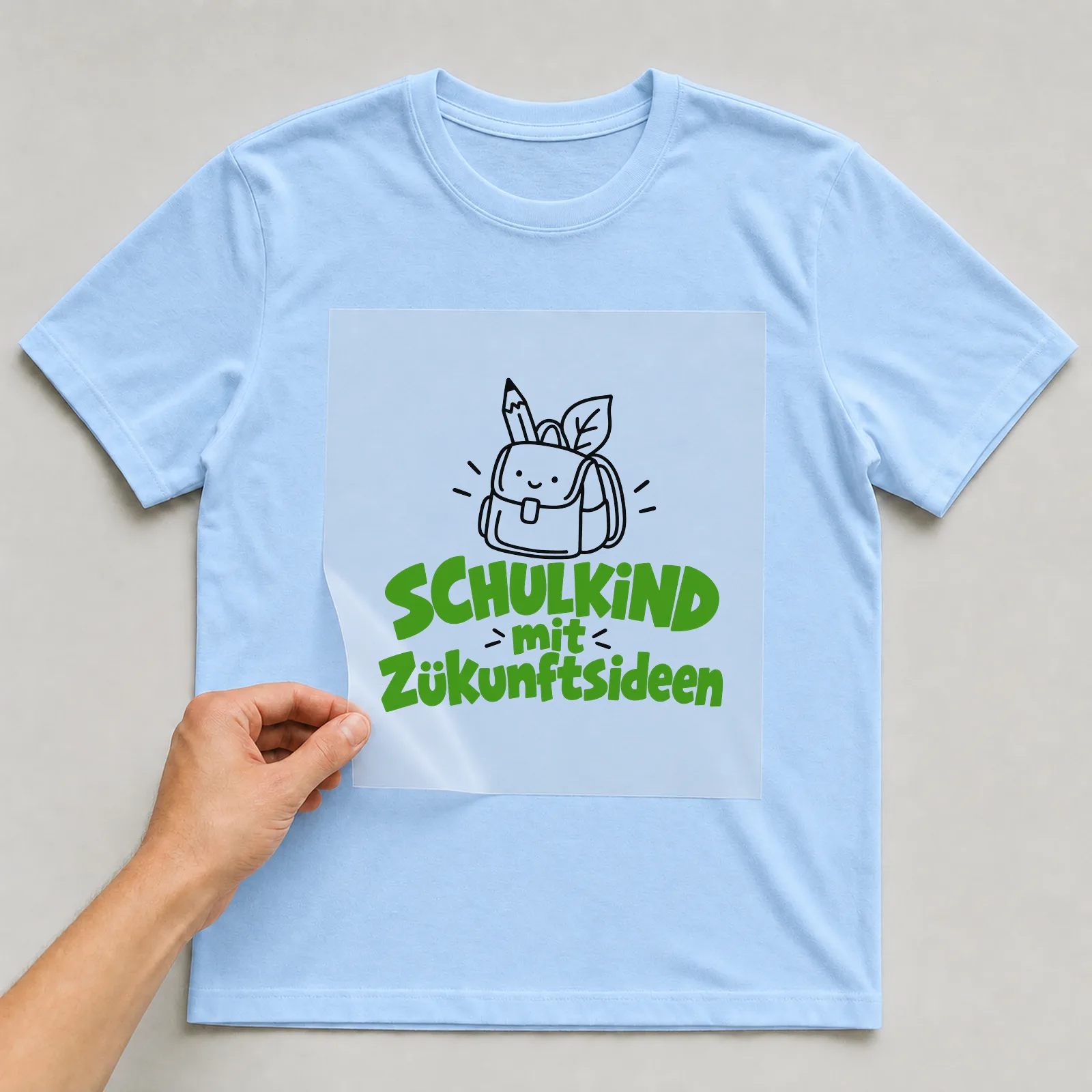 Bügelbild „Schulkind mit Zukunftsideen“ auf hellblauem T-Shirt, Folie wird aufgelegt