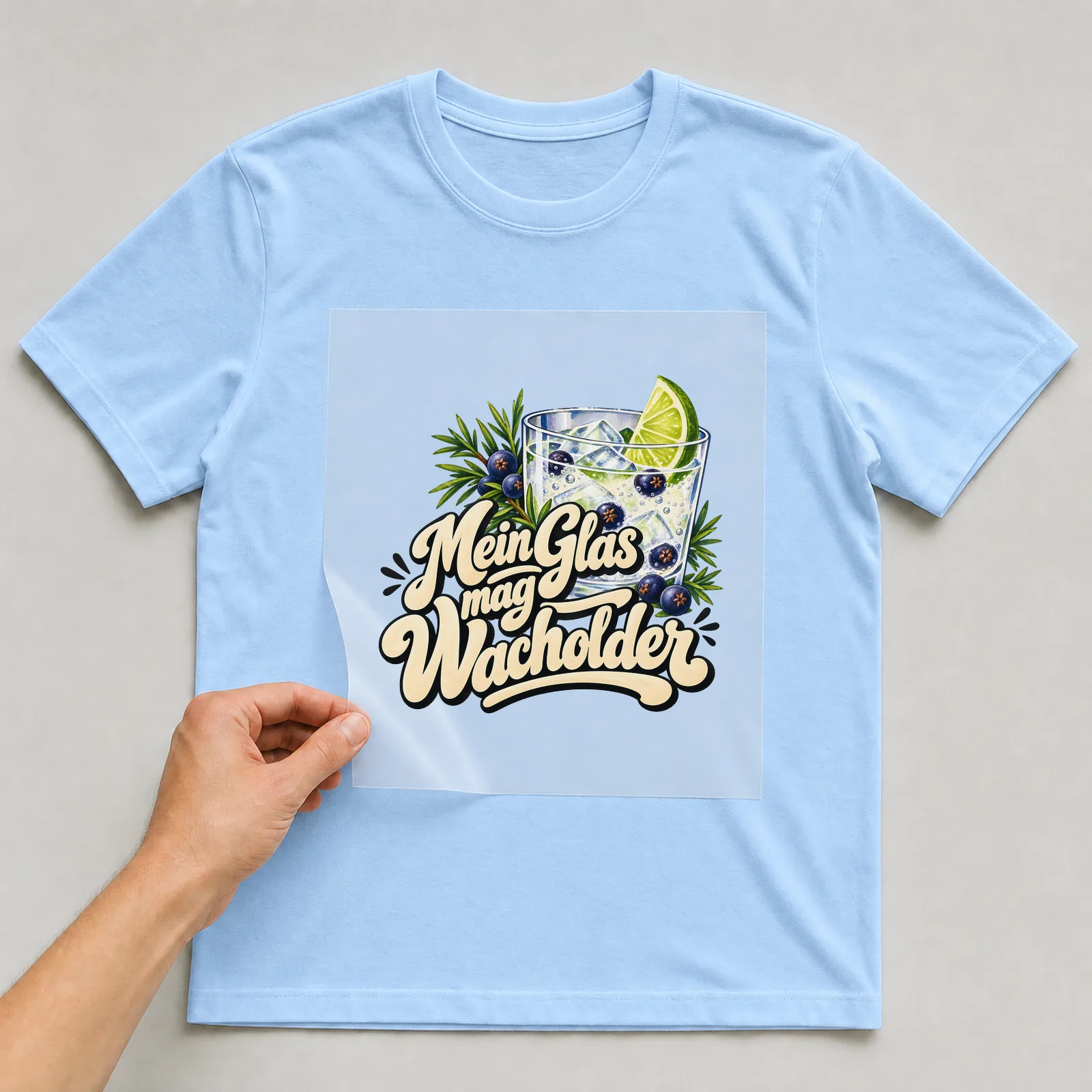 Bügelbild „Mein Glas mag Wacholder“ auf hellblauem T-Shirt, Folie wird aufgelegt