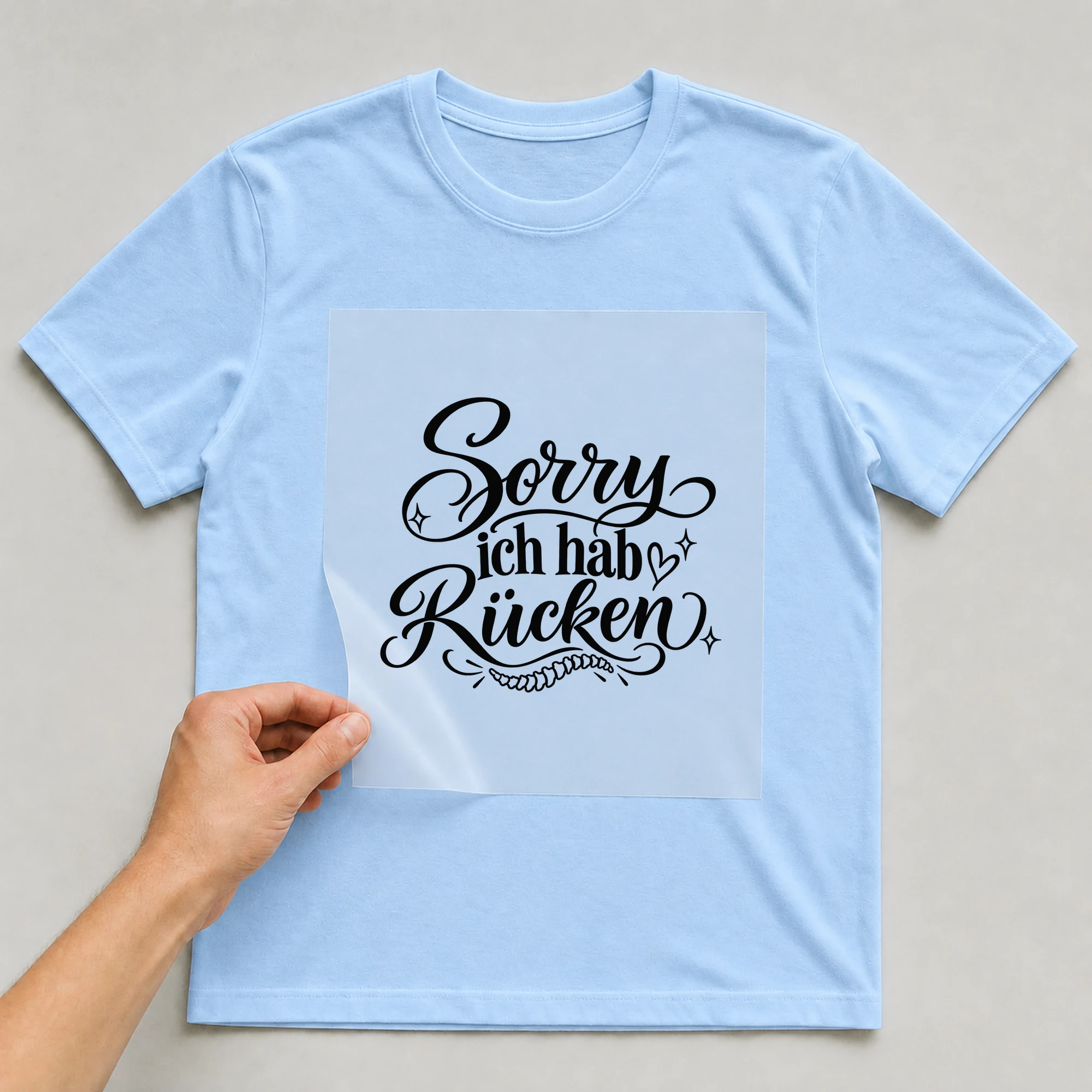 Bügelbild „Sorry ich hab Rücken“ auf babyblauem T-Shirt, Folie wird aufgelegt