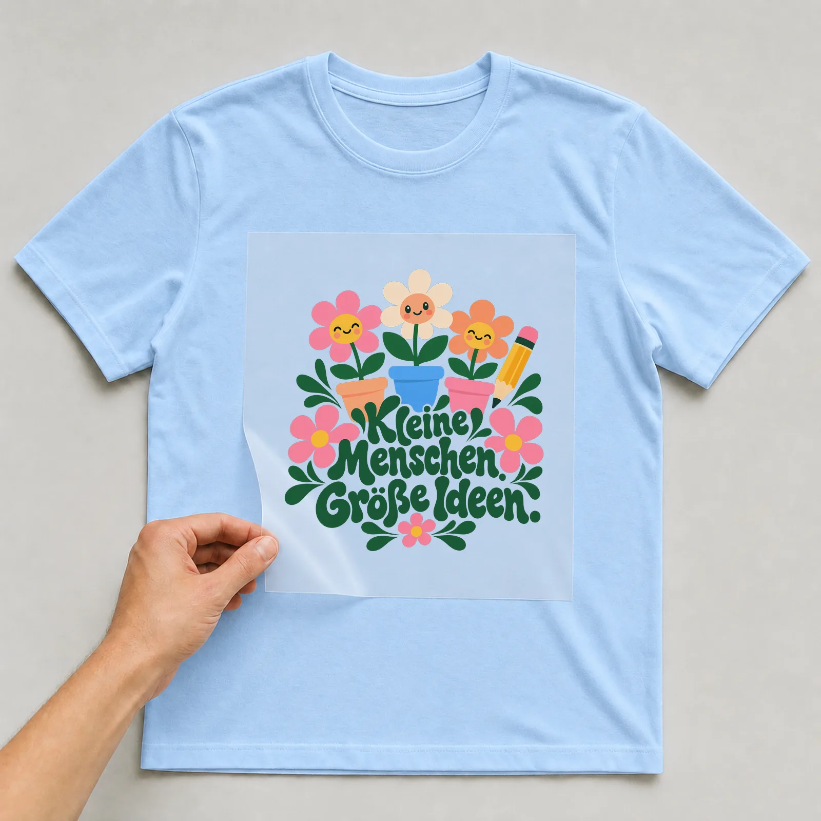 Bügelbild „Kleine Menschen. Große Ideen.“ auf hellblauem T-Shirt, Folie wird aufgelegt