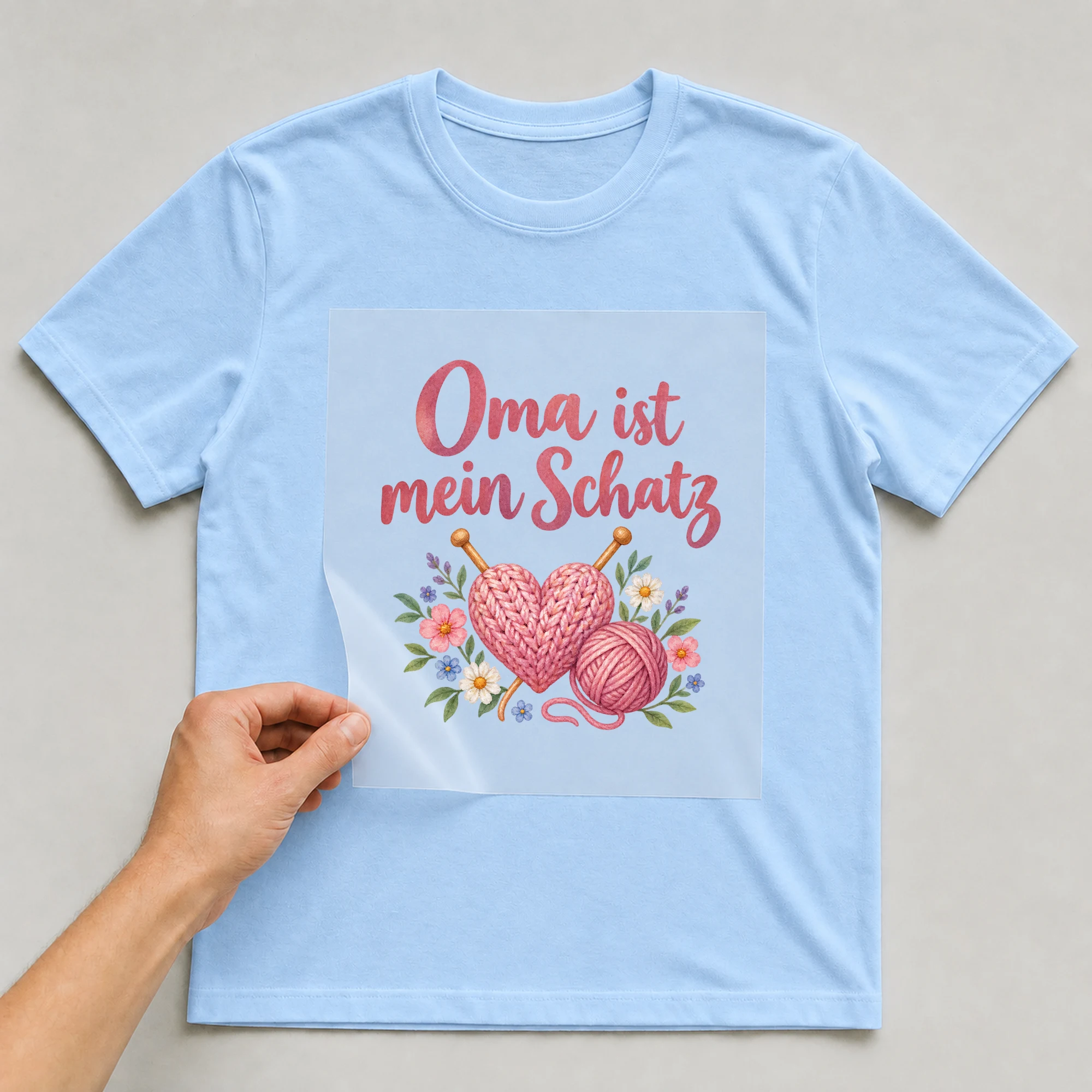 Bügelbild „Oma ist mein Schatz“ auf babyblauem T-Shirt, Folie wird aufgelegt