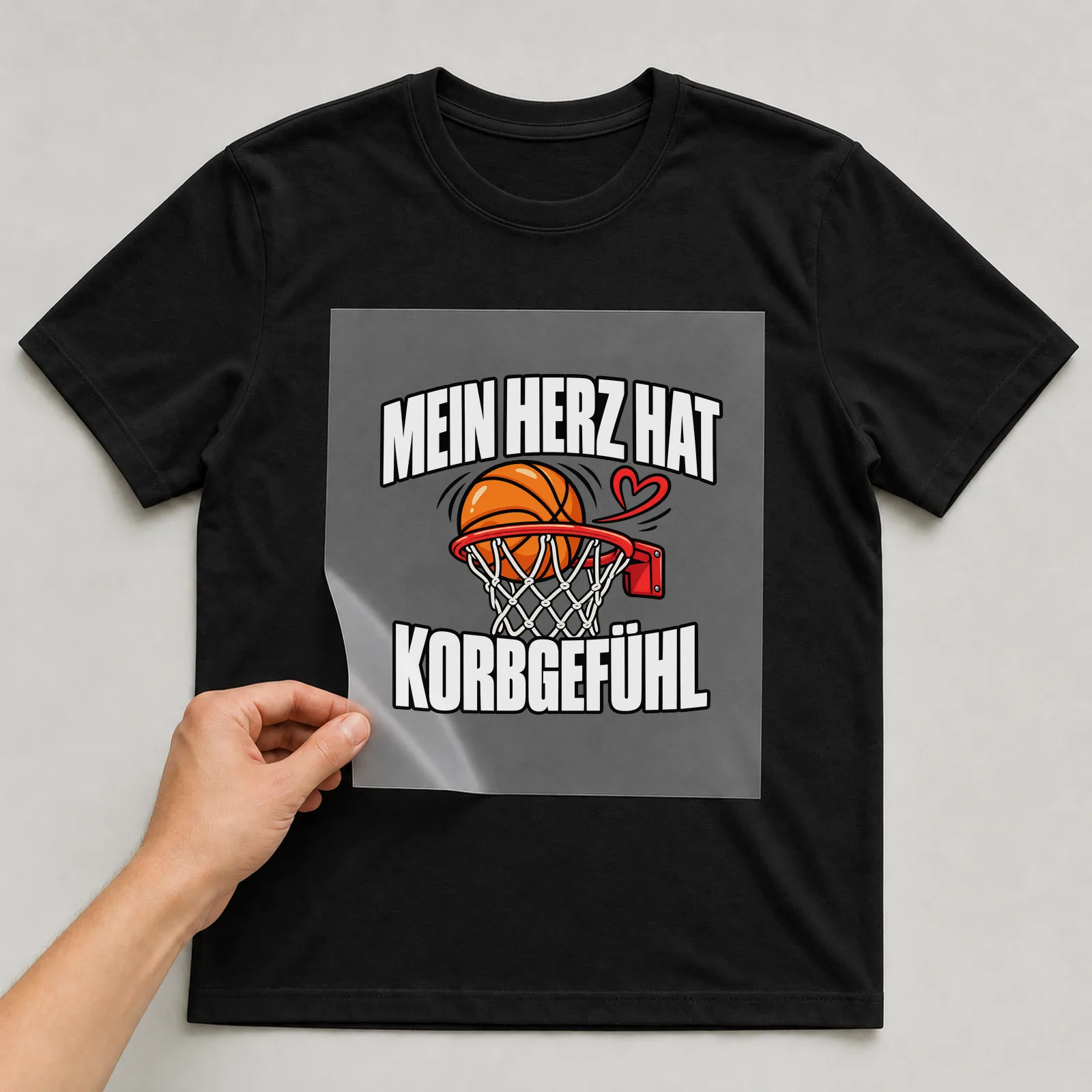 Bügelbild „Mein Herz hat Korbgefühl“ auf schwarzem T-Shirt, Folie wird aufgelegt