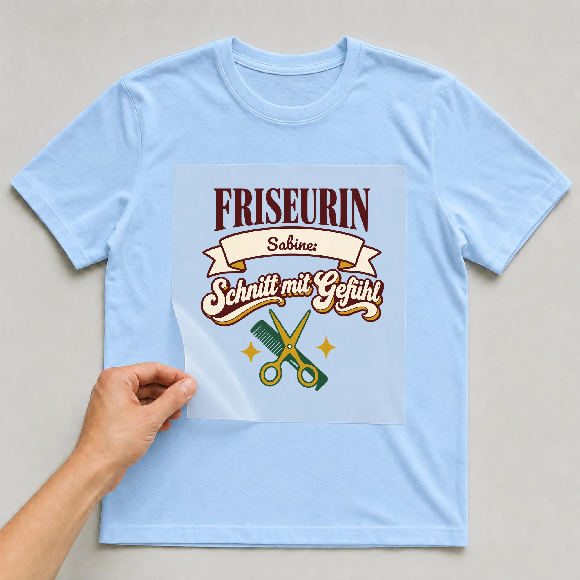 Bügelbild Friseurin: Schnitt mit Gefühl mit Name auf hellblauem T-Shirt, Folie wird aufgelegt