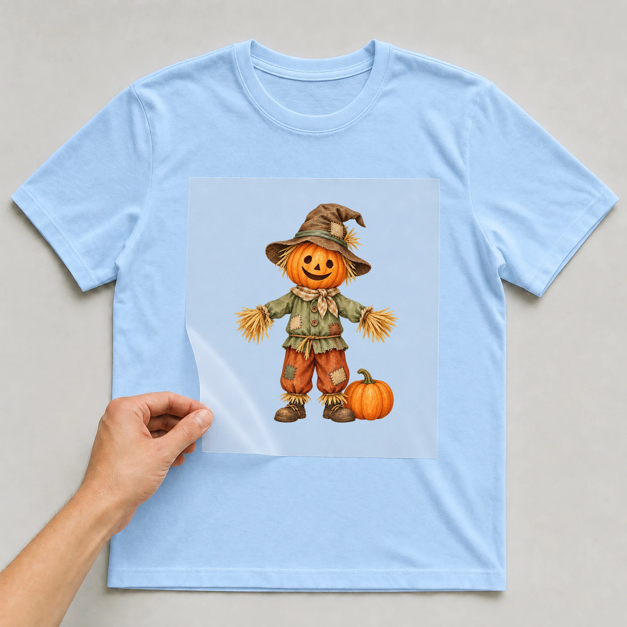Bügelbild „Kürbis Vogelscheuche“ auf babyblauem T-Shirt, Folie wird aufgelegt
