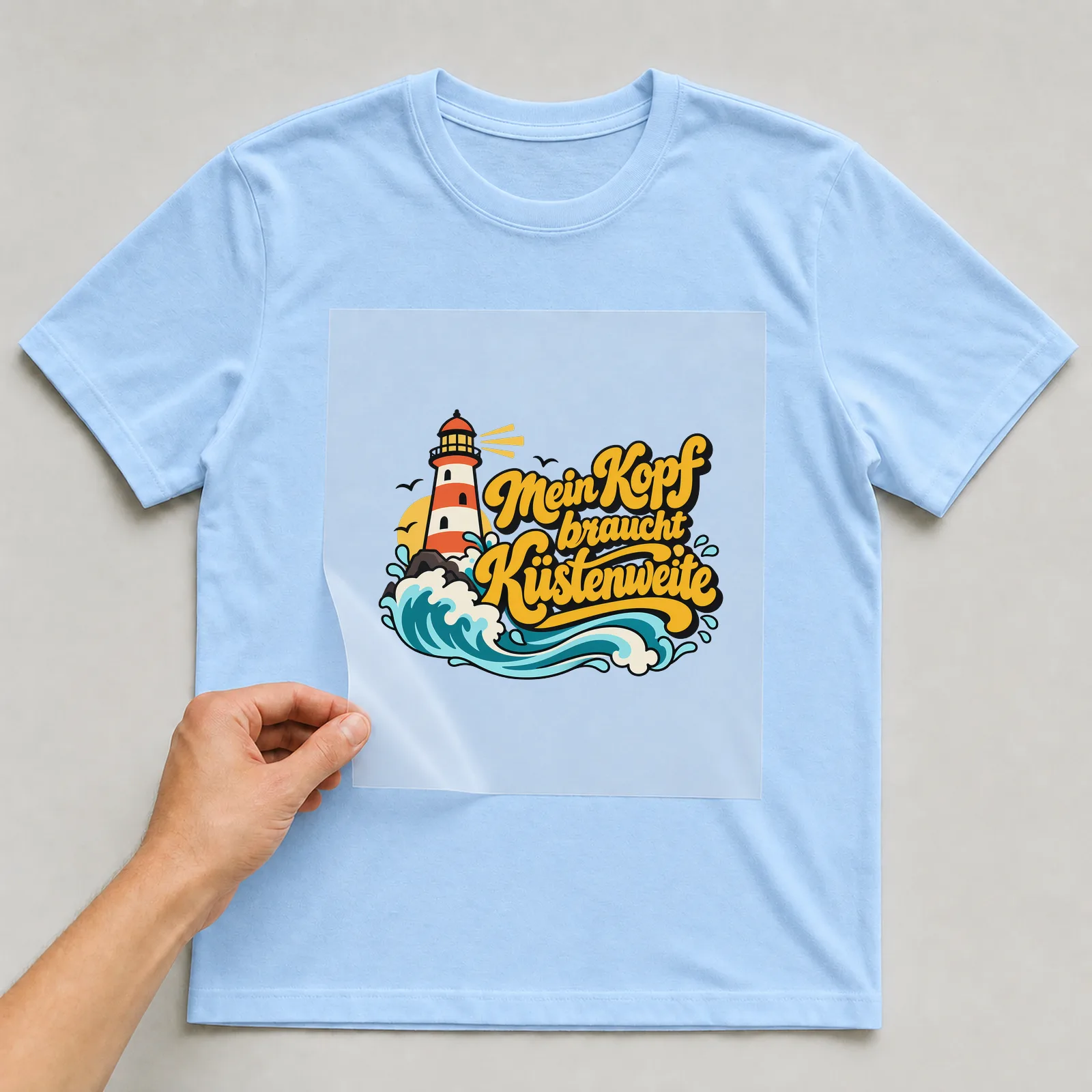 Bügelbild „Mein Kopf braucht Küstenweite“ auf hellblauem T-Shirt, Folie wird aufgelegt