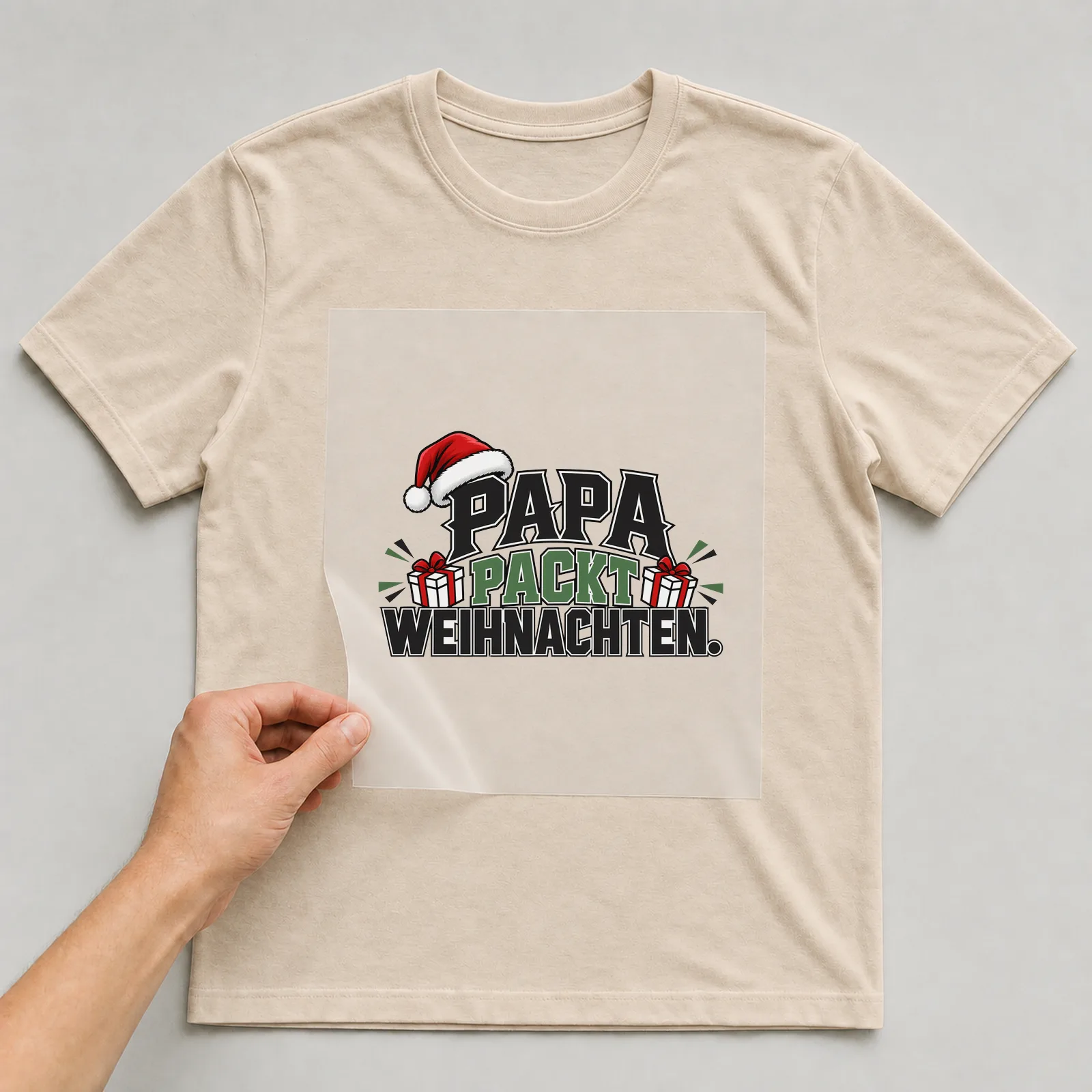 Bügelbild „Papa packt Weihnachten“ auf beigem T-Shirt, Folie wird aufgelegt