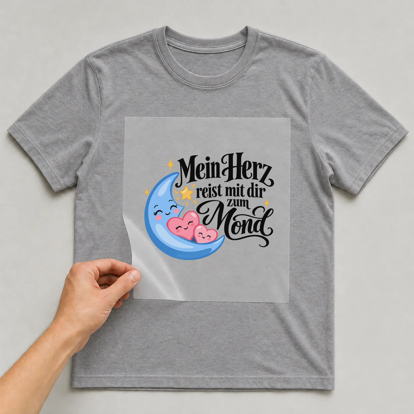 Bügelbild „Mein Herz reist mit dir zum Mond“ auf grauem T-Shirt, Folie wird aufgelegt