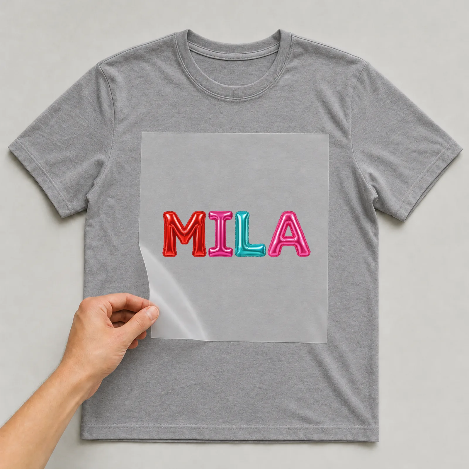Bügelbild Ballon-Buchstaben mit Name auf grauem T-Shirt, Folie wird aufgelegt