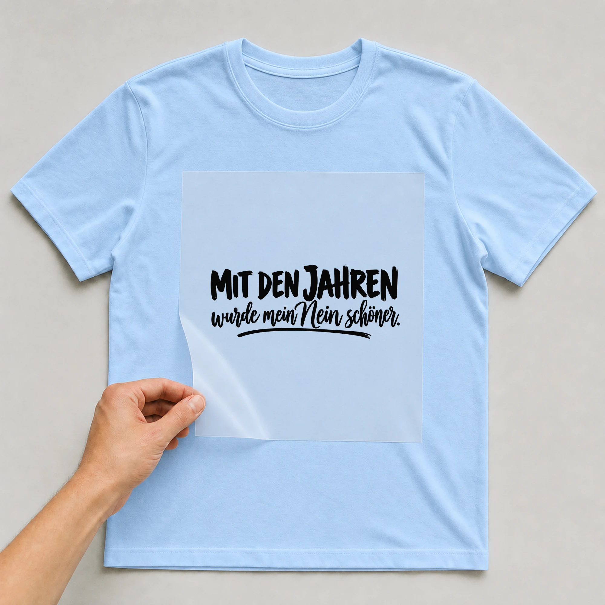 Bügelbild „Mit den Jahren wurde mein Nein schöner.“ auf babyblauem T-Shirt, Folie wird aufgelegt