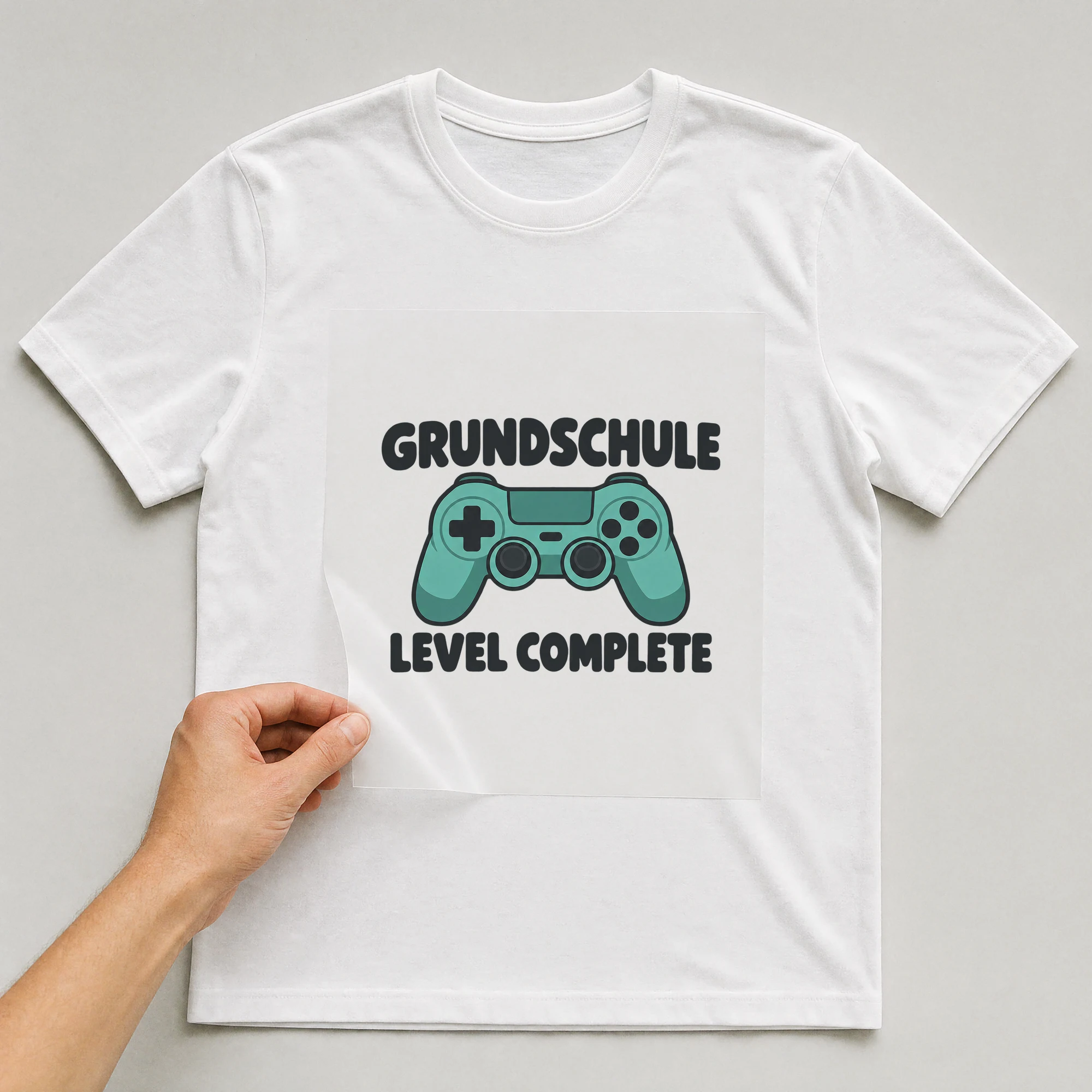 Bügelbild „Grundschule Level Complete“ auf weißem T-Shirt, Folie wird aufgelegt