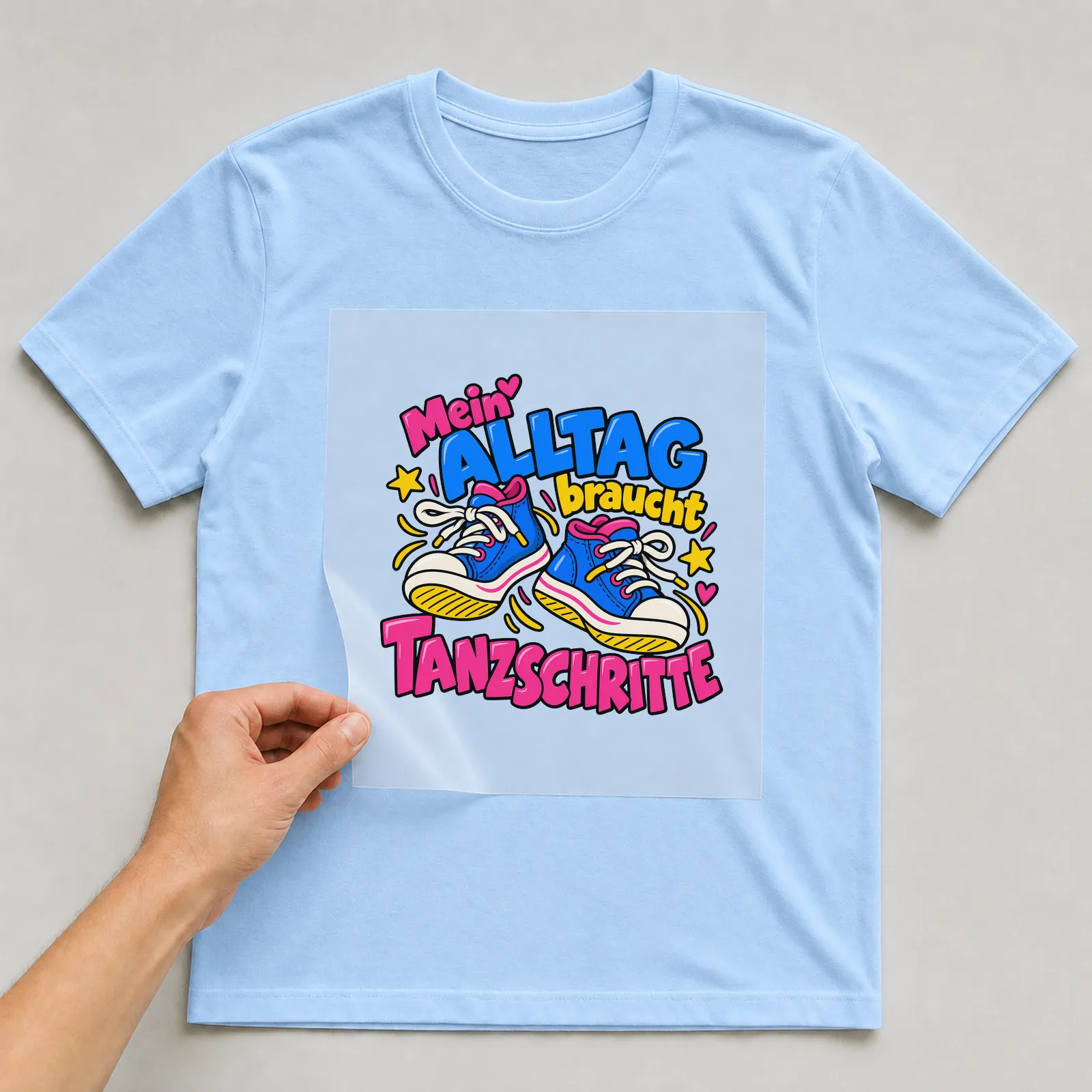 Bügelbild „Mein Alltag braucht Tanzschritte“ auf hellblauem T-Shirt, Folie wird aufgelegt