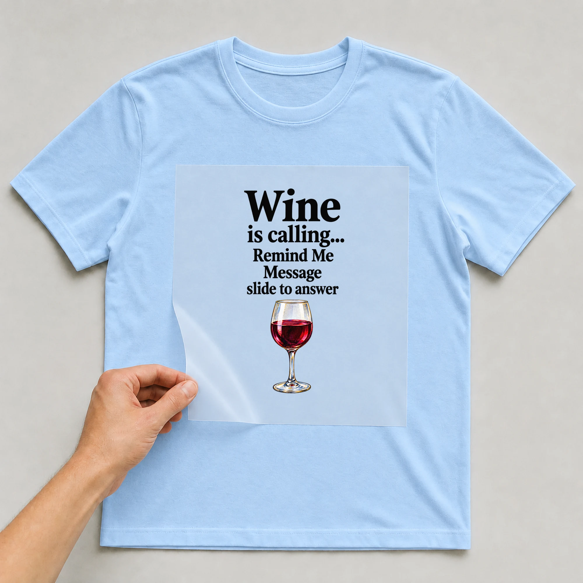 Bügelbild „Wine is calling... Remind Me Message slide to answer“ auf babyblauem T-Shirt, Folie wird aufgelegt