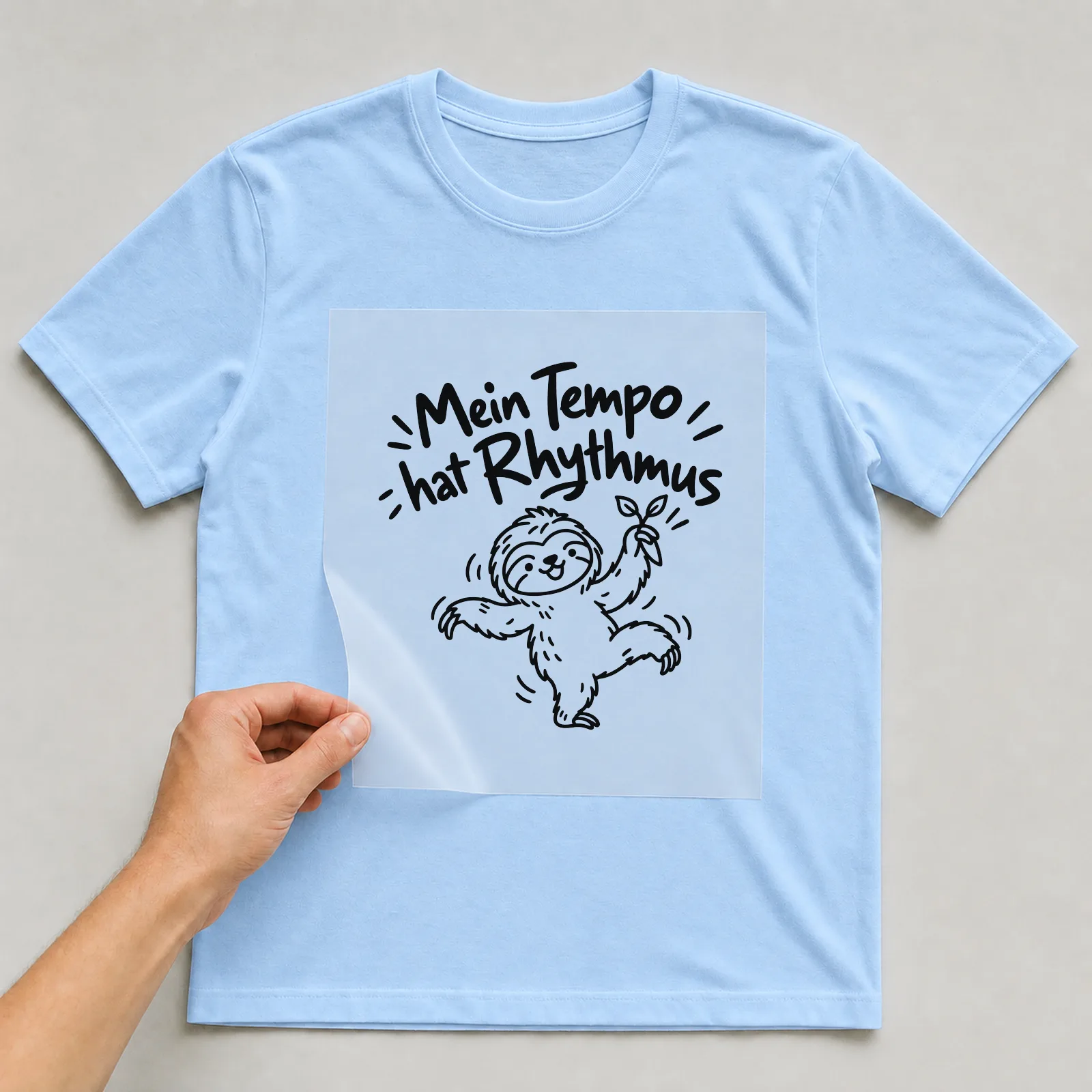 Bügelbild „Mein Tempo hat Rhythmus“ auf hellblauem T-Shirt, Folie wird aufgelegt