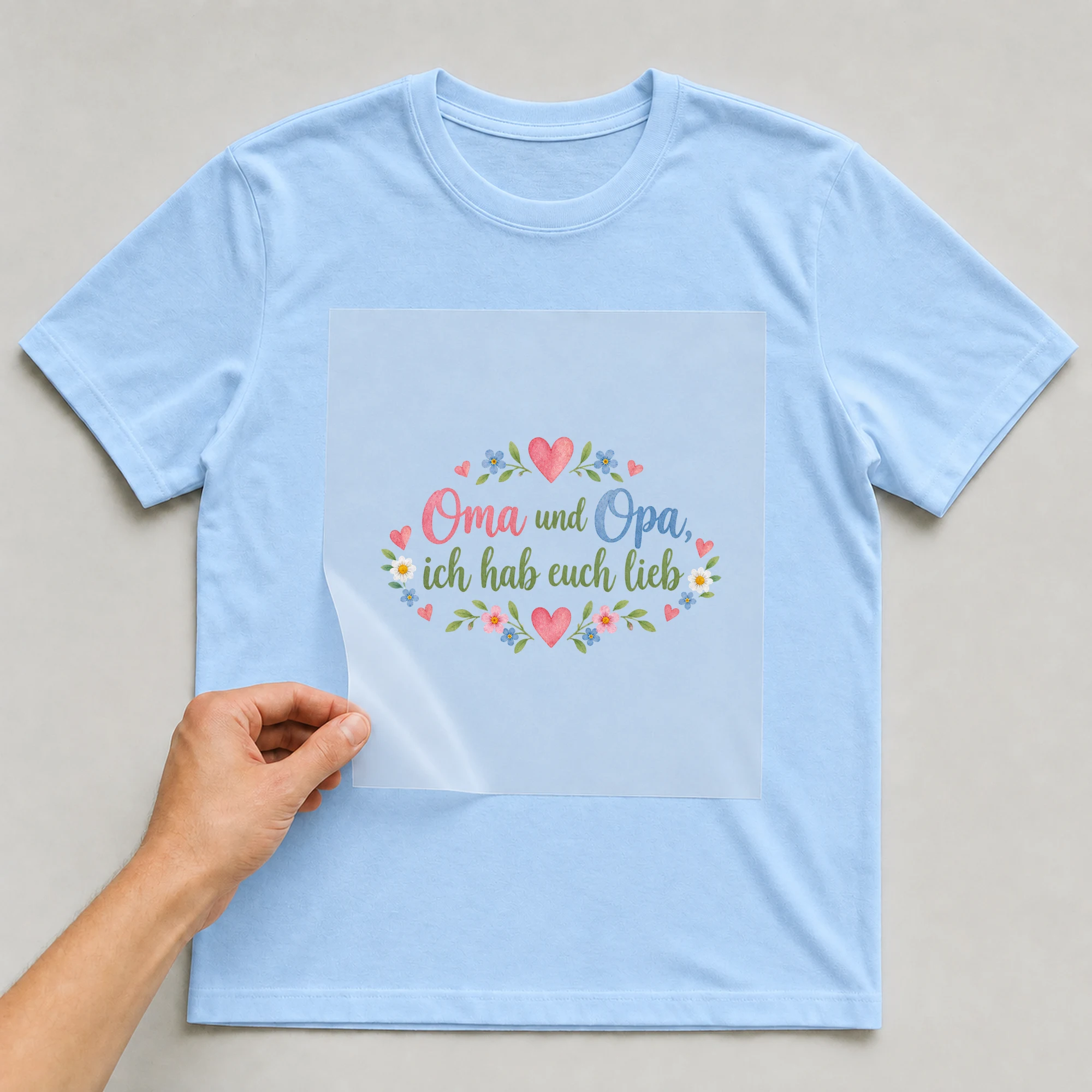 Bügelbild „Oma und Opa, ich hab euch lieb“ auf babyblauem T-Shirt, Folie wird aufgelegt