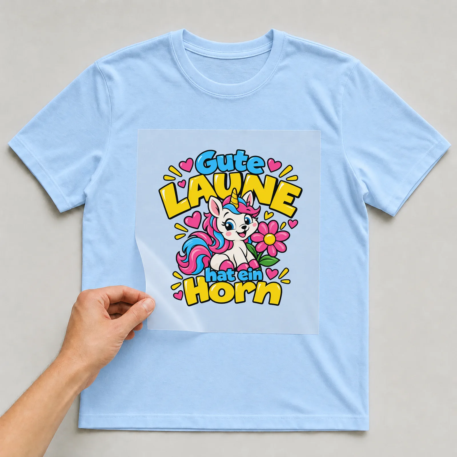 Bügelbild „Gute Laune hat ein Horn“ auf hellblauem T-Shirt, Folie wird aufgelegt