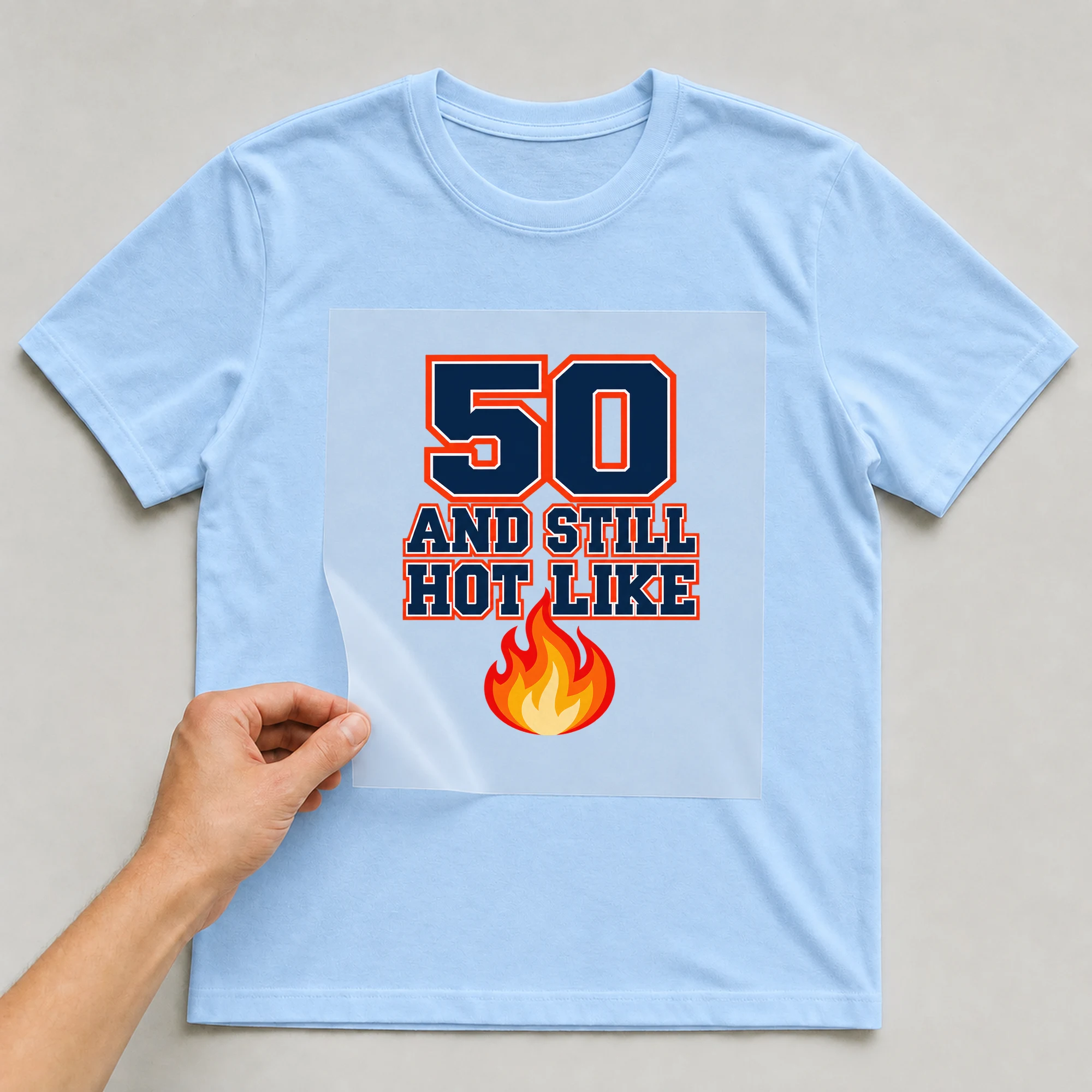 Bügelbild „50 And Still Hot Like“ auf babyblauem T-Shirt, Folie wird aufgelegt