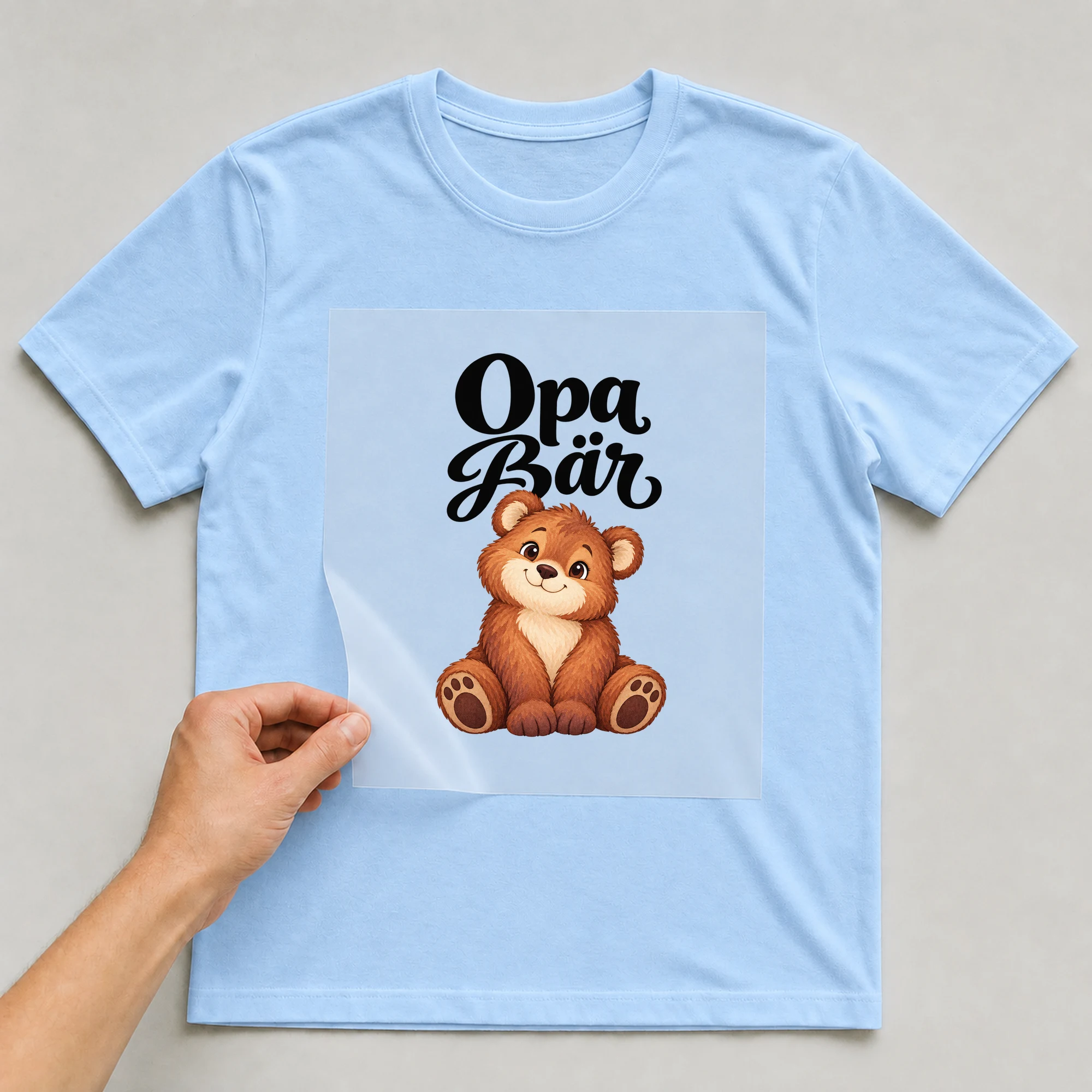 Bügelbild „Opa Bär“ auf babyblauem T-Shirt, Folie wird aufgelegt