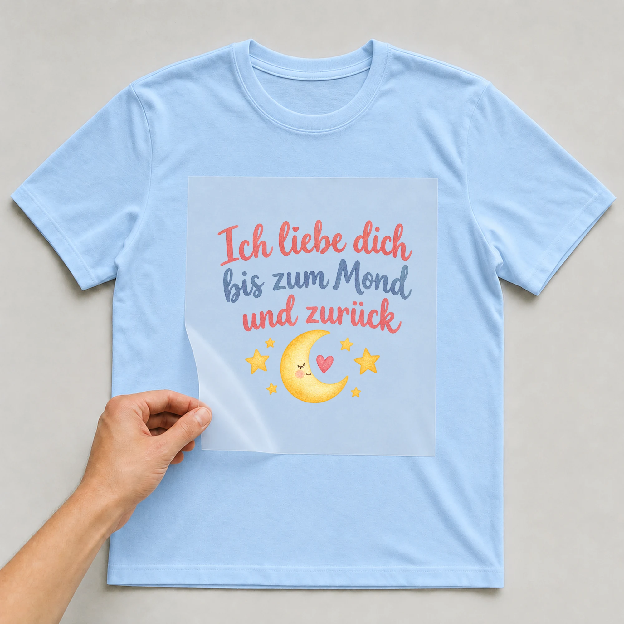 Bügelbild „Ich liebe dich bis zum Mond und zurück“ auf babyblauem T-Shirt, Folie wird aufgelegt