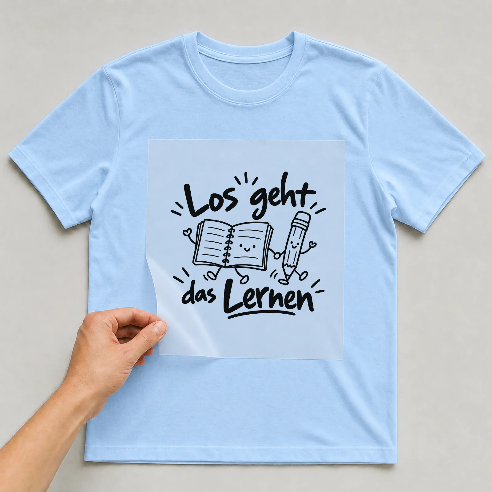 Bügelbild „Los geht das Lernen“ auf hellblauem T-Shirt, Folie wird aufgelegt