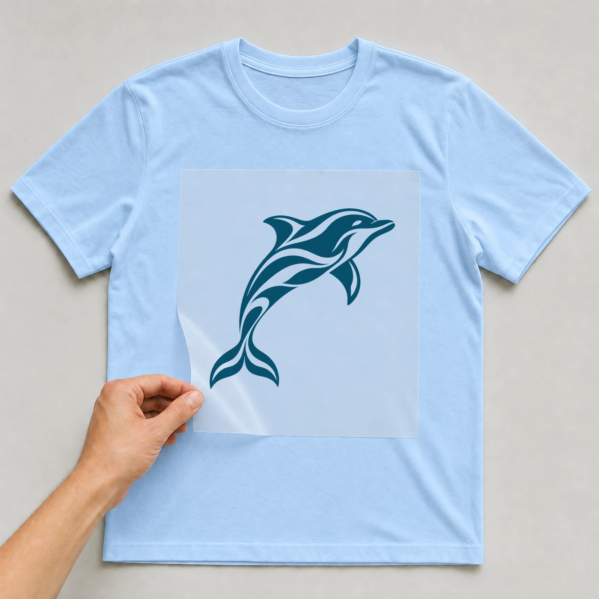 Bügelbild „Delfin in Blau“ auf babyblauem T-Shirt, Folie wird aufgelegt